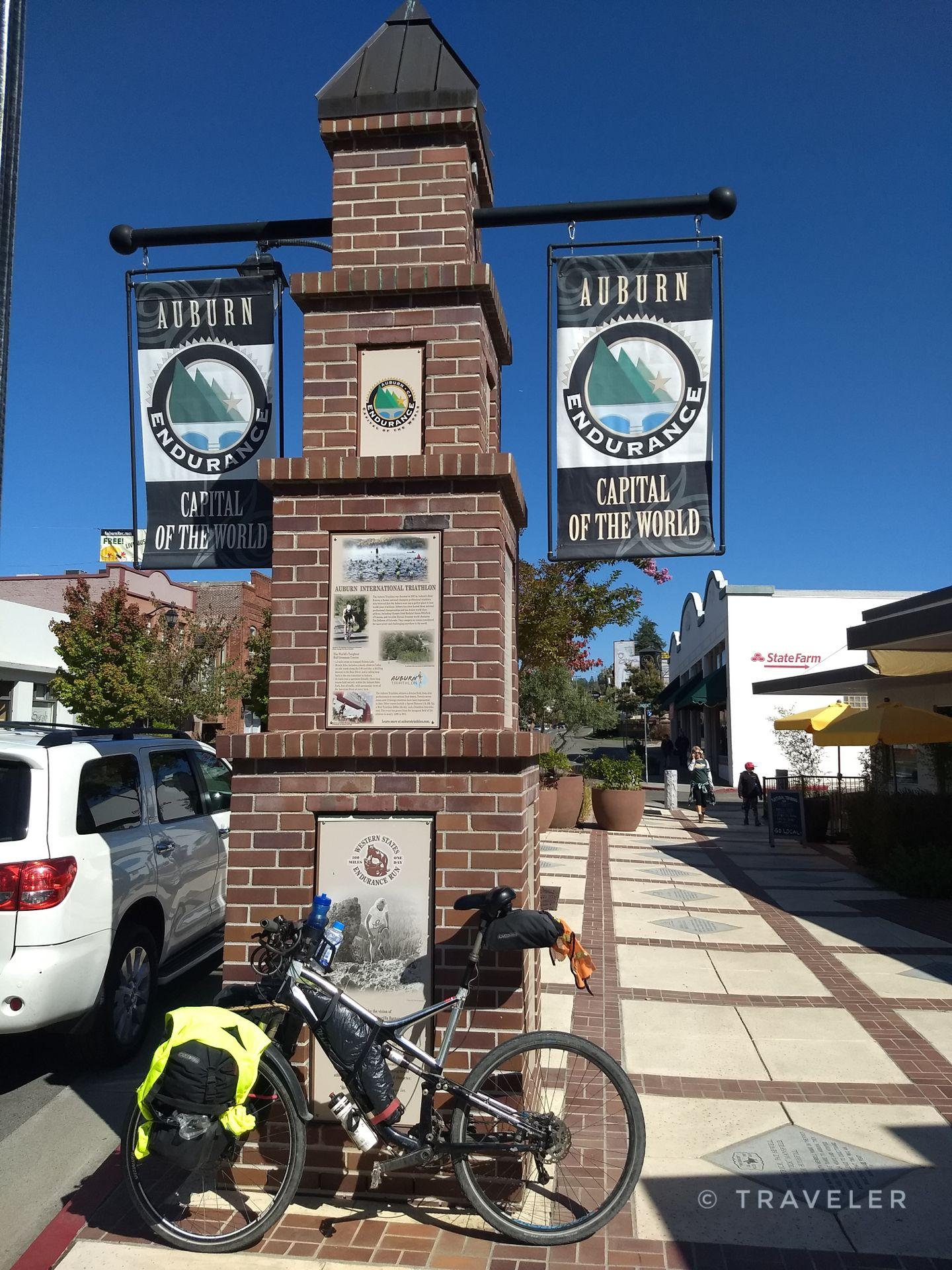 A bicycle parked by a brick monument with banners on a sunny street.