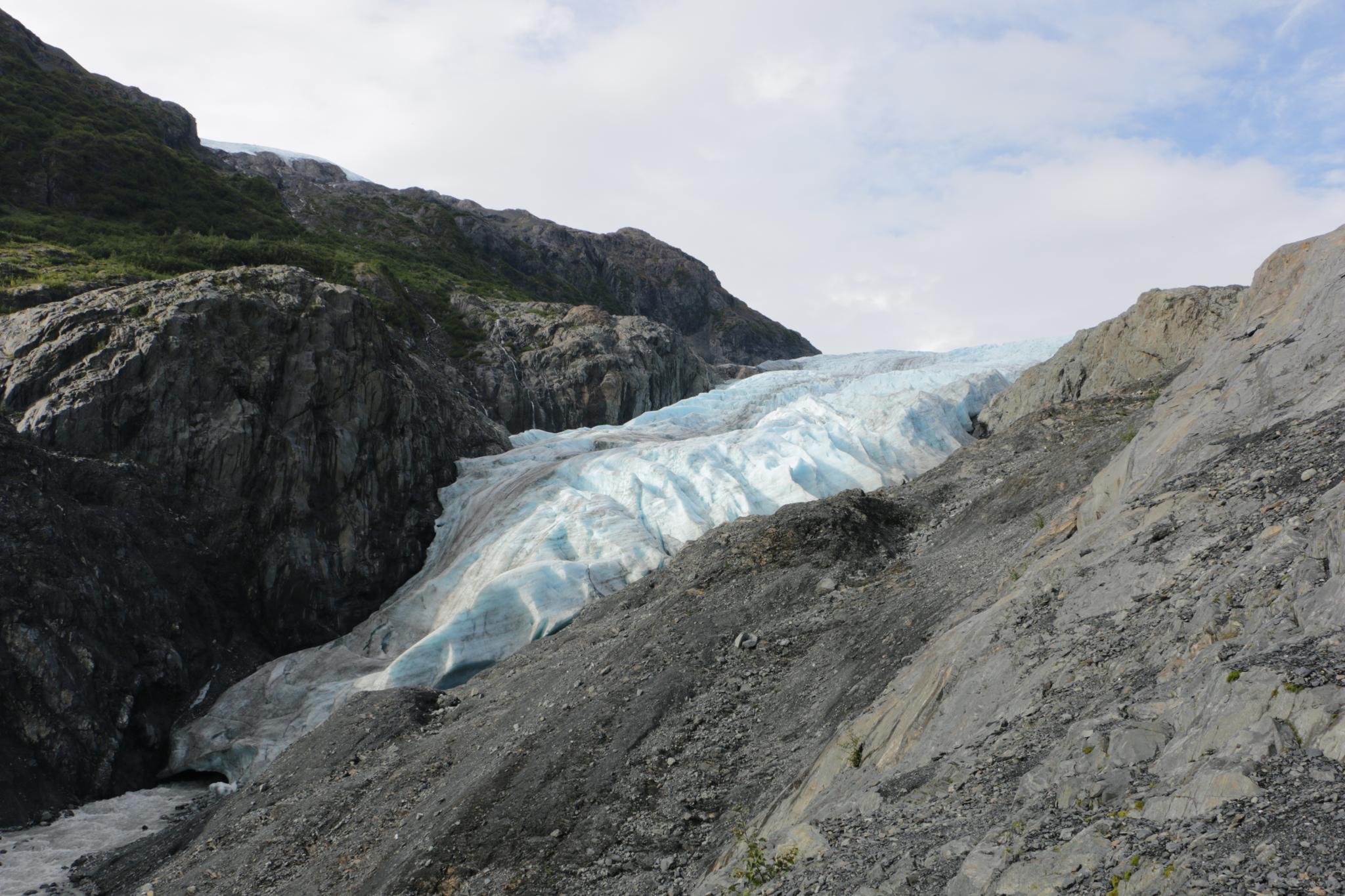 A large blue glacier descends through a rocky, rugged mountain valley.