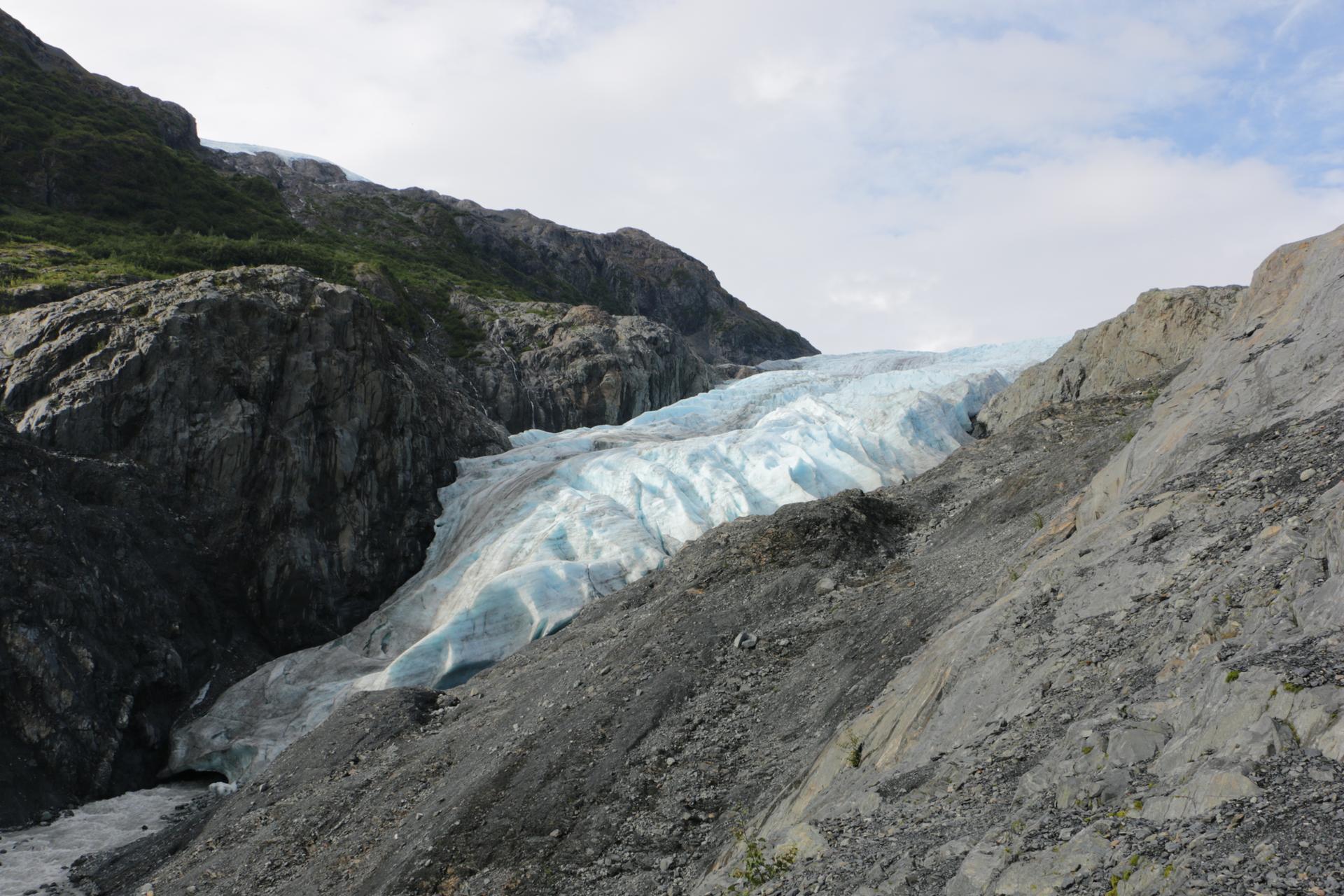 A large blue glacier descends through a rocky, rugged mountain valley.