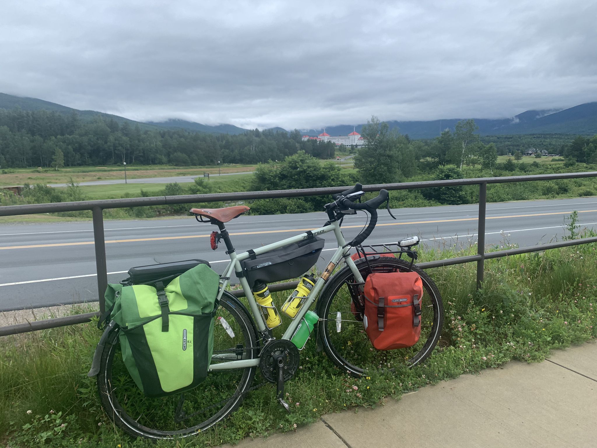 Bicycle with green and orange bags parked by a road, mountains in distance. - Old Cherry Mountain Road, Valley Road, & Jefferson Notch Road gravel loop