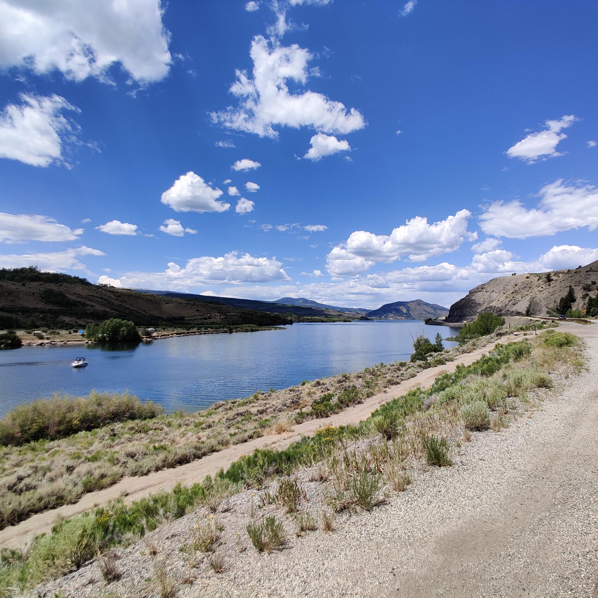 Bright day over a large lake with a boat, arid hills, and a gravel path.