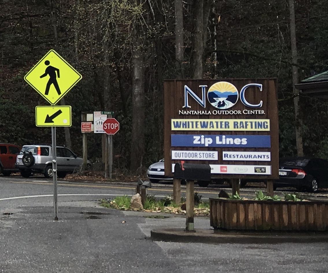 Roadside signs for outdoor activities like rafting and zip lines, cars parked.