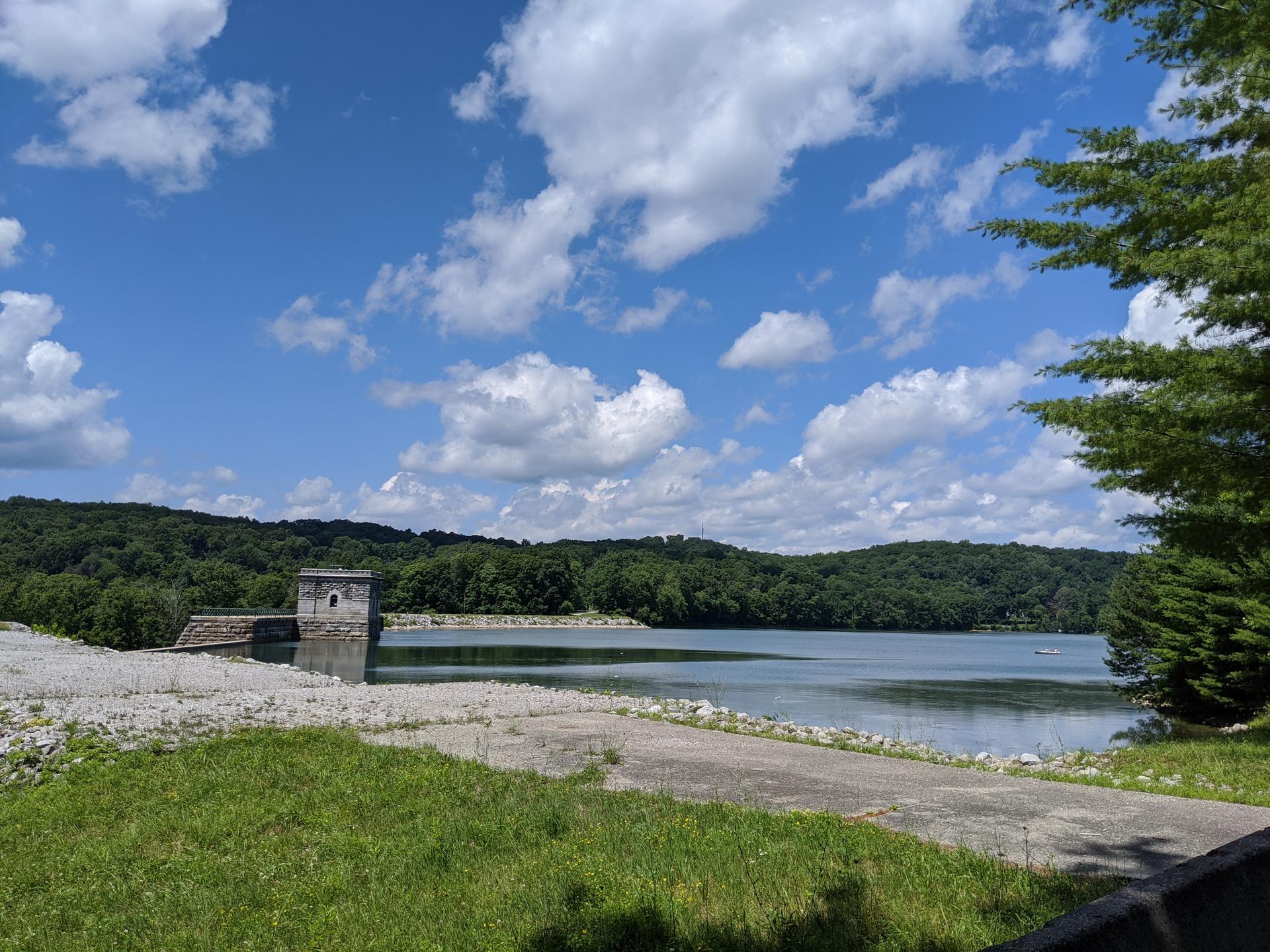 A lake with a stone tower and forested hills under a bright, cloudy sky.