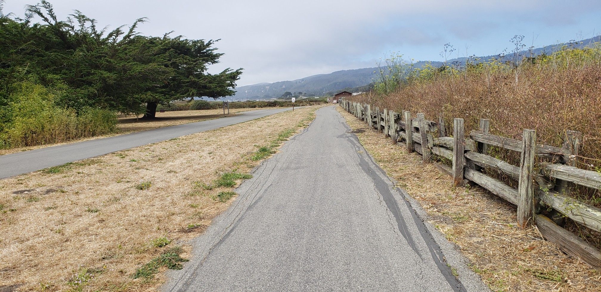 Paved path next to a wooden fence with dry grass and hills. - Francis Beach (Half Moon Bay) – Higgins Canyon Road loop from Half Moon Bay