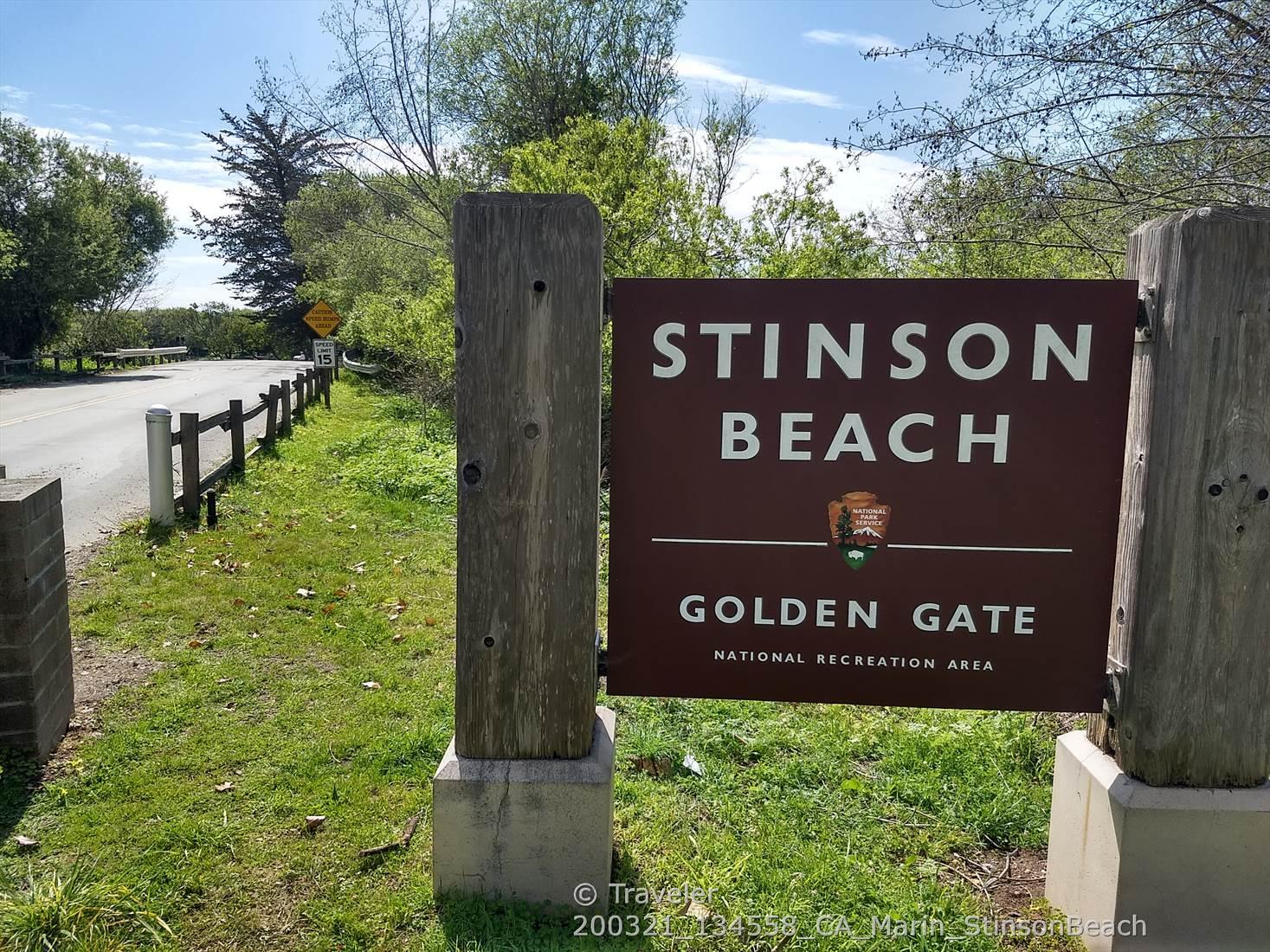 Brown wooden sign on posts next to a grassy area and a road.