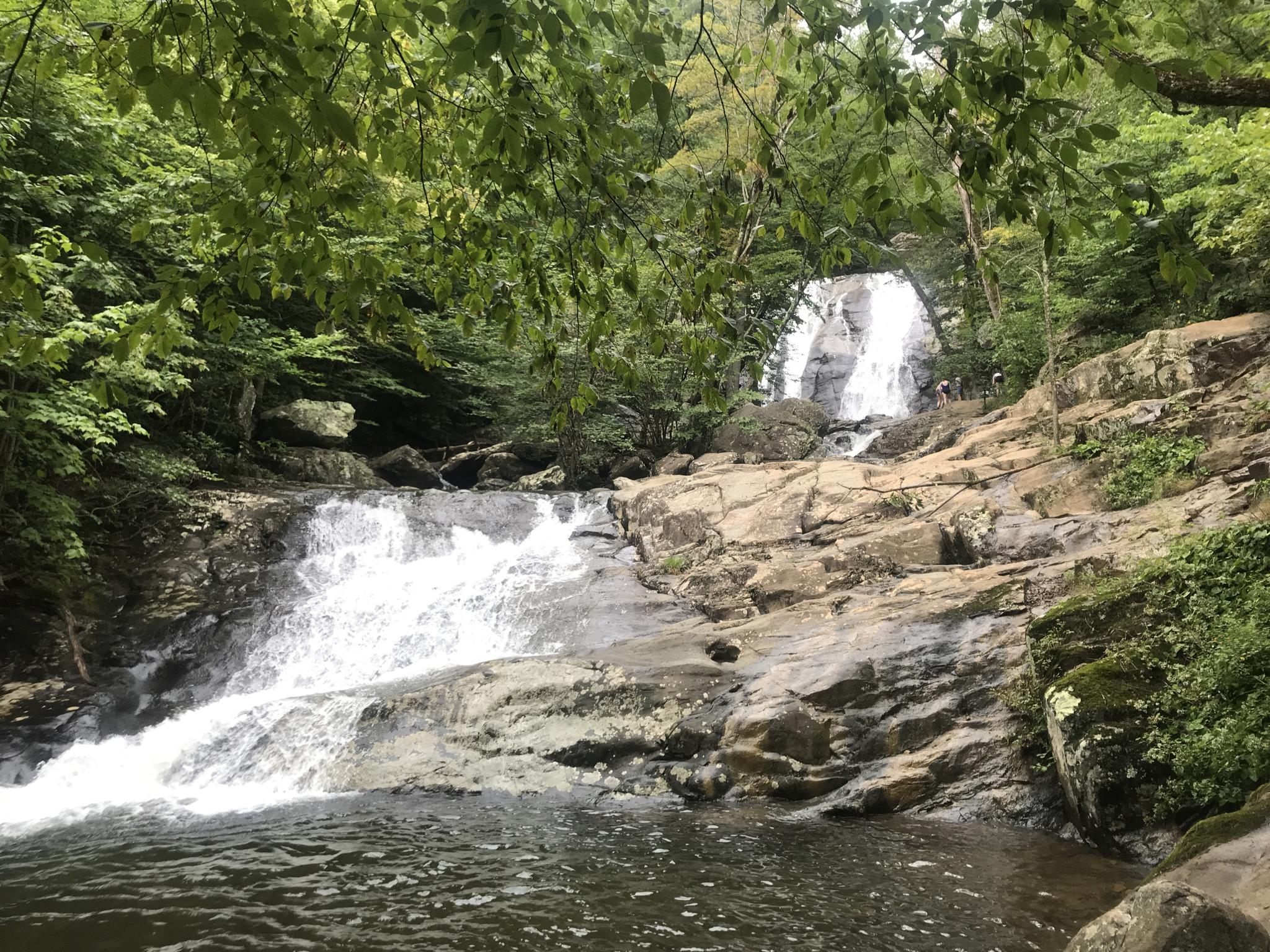 Multi-tiered waterfall cascading over rocks into a pool, people nearby.