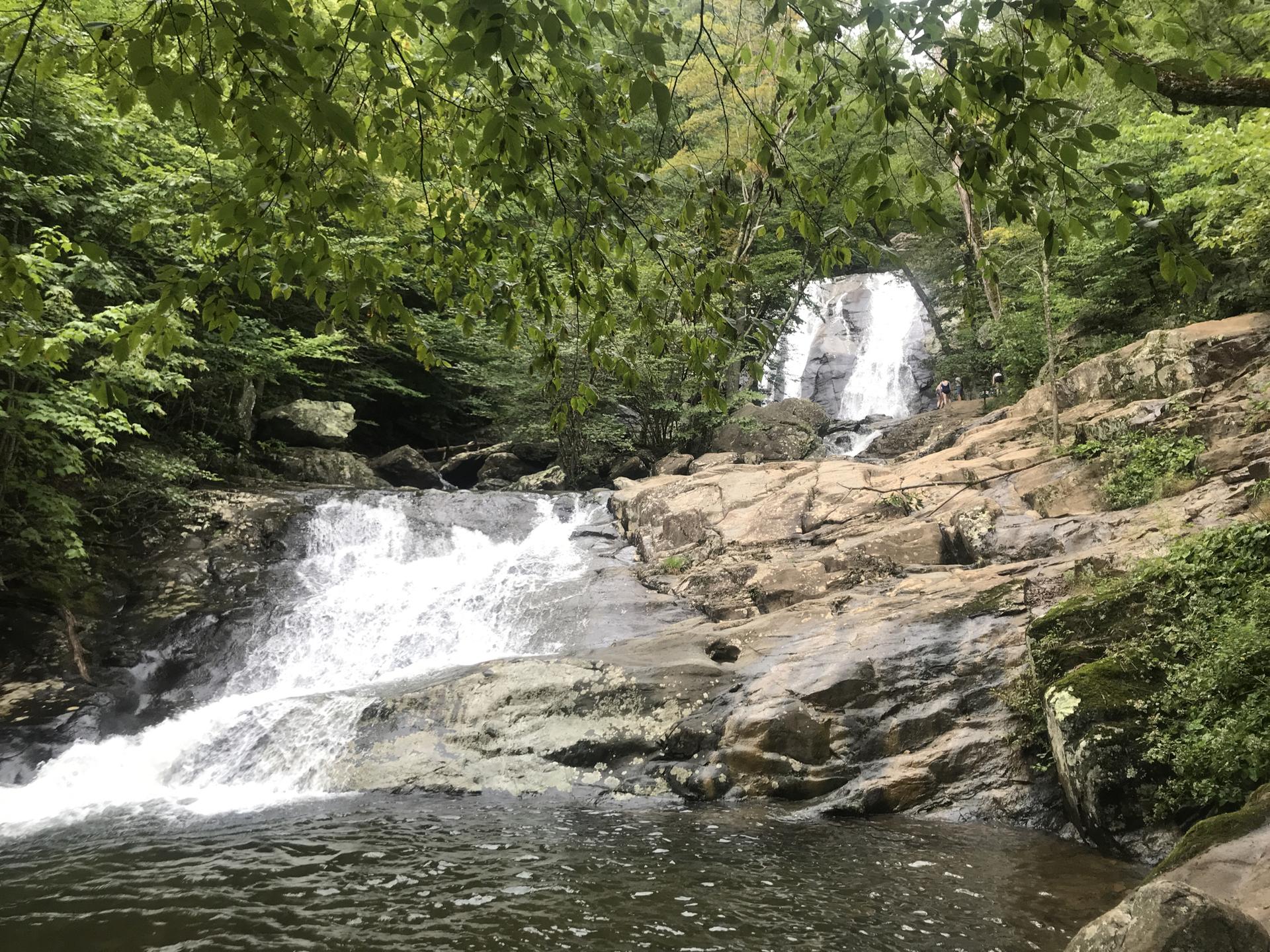 Multi-tiered waterfall cascading over rocks into a pool, people nearby.