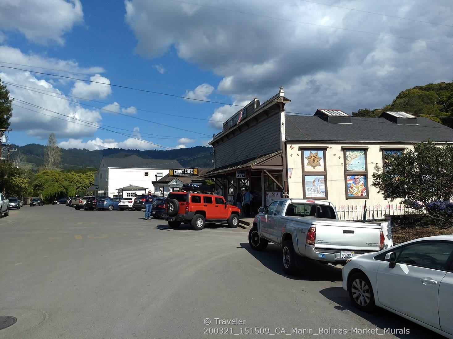 Street scene with buildings, parked cars, and distant hills under a bright sky.