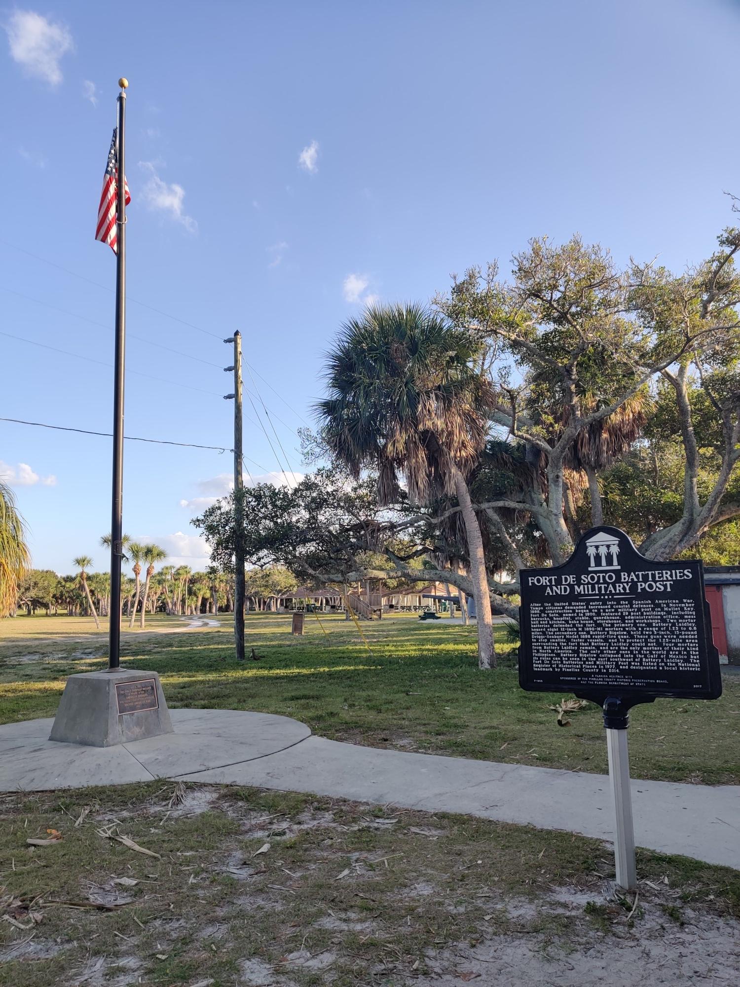 American flag on a pole next to a historical marker in a grassy park.