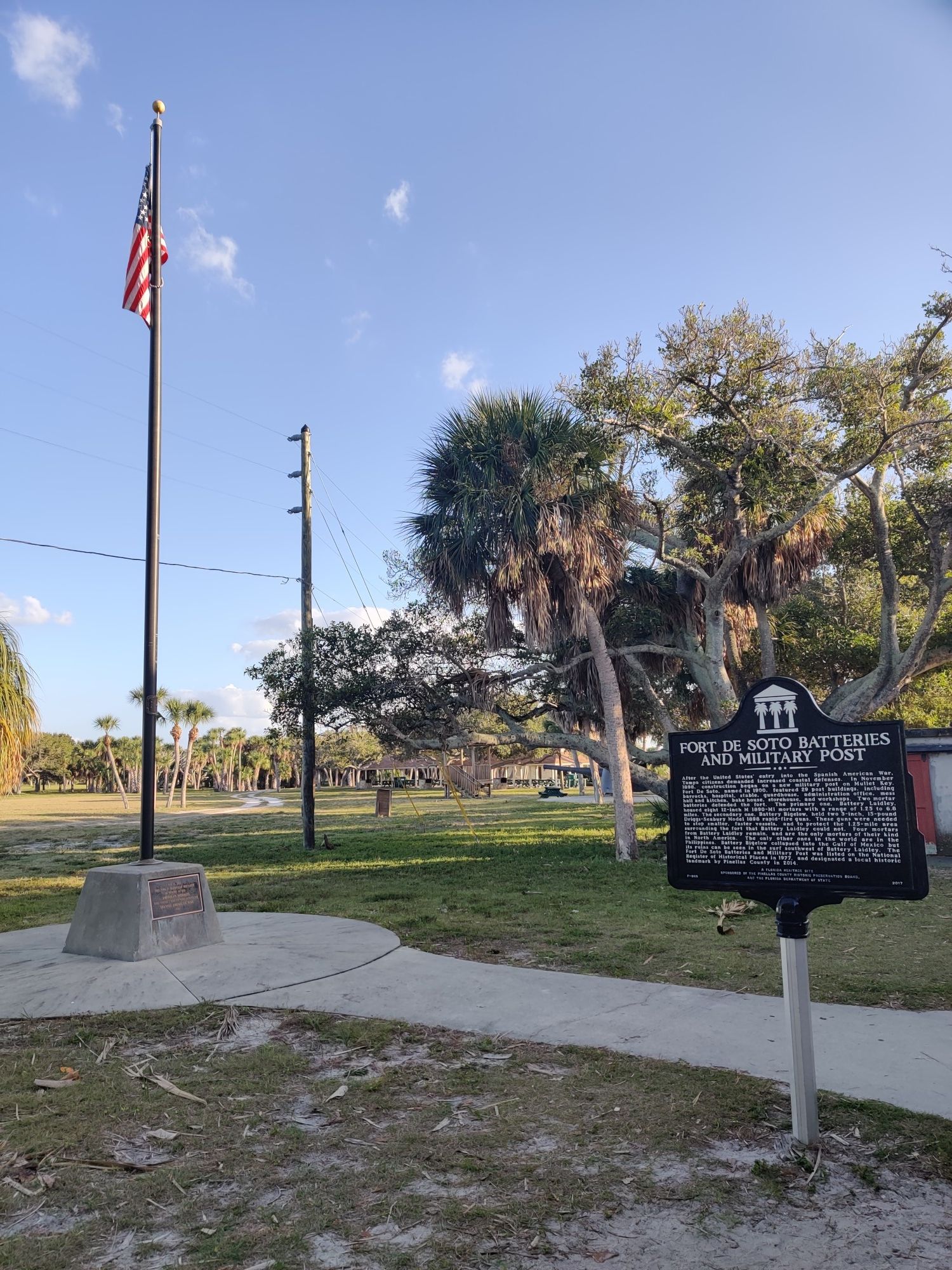 American flag on a pole next to a historical marker in a grassy park. - Fort De Soto Recreational Trail