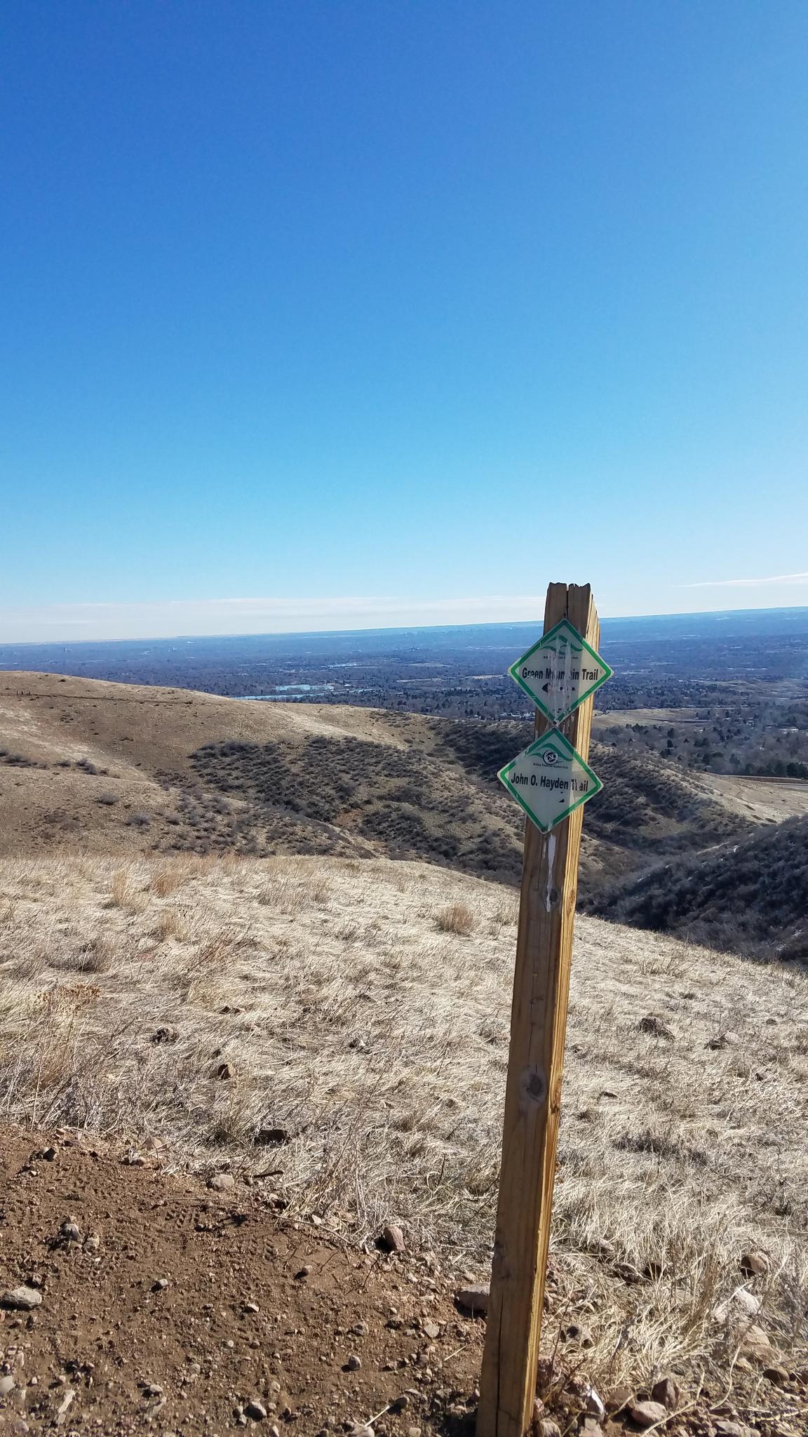 Trail marker on a dry hillside overlooking a vast, sunny landscape.