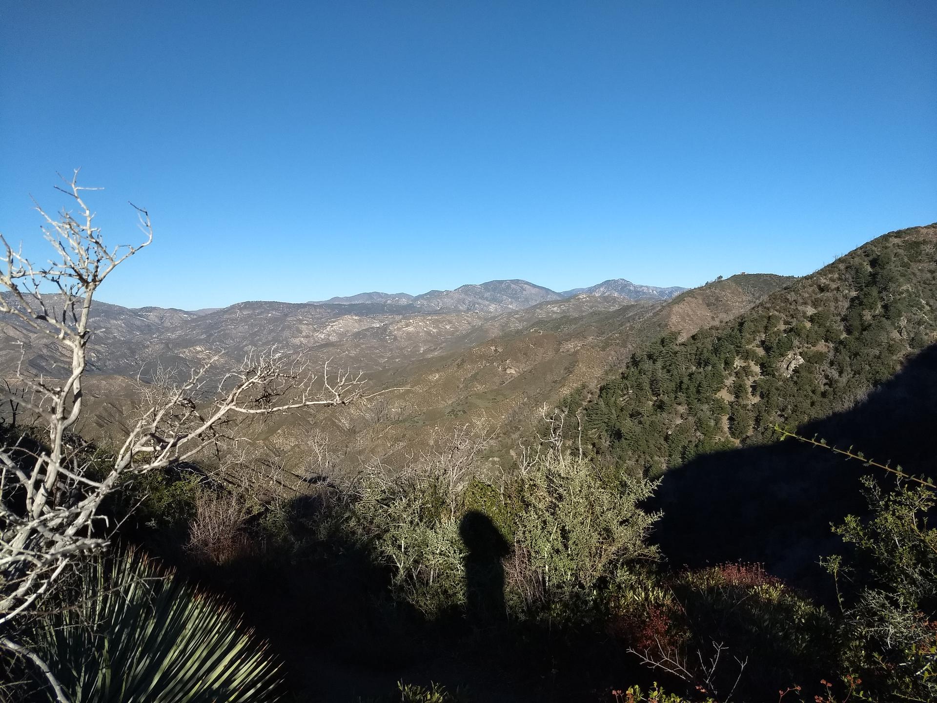 Panoramic view of dry, rugged mountains with a person's shadow in the foreground.