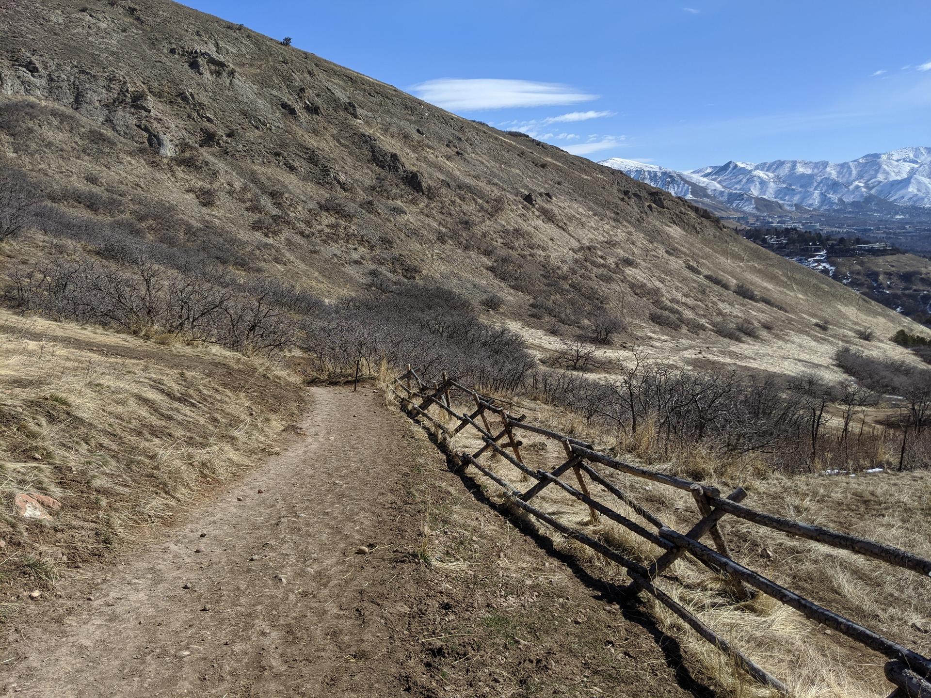 Dirt path alongside a wooden fence on a dry, sunny hillside.