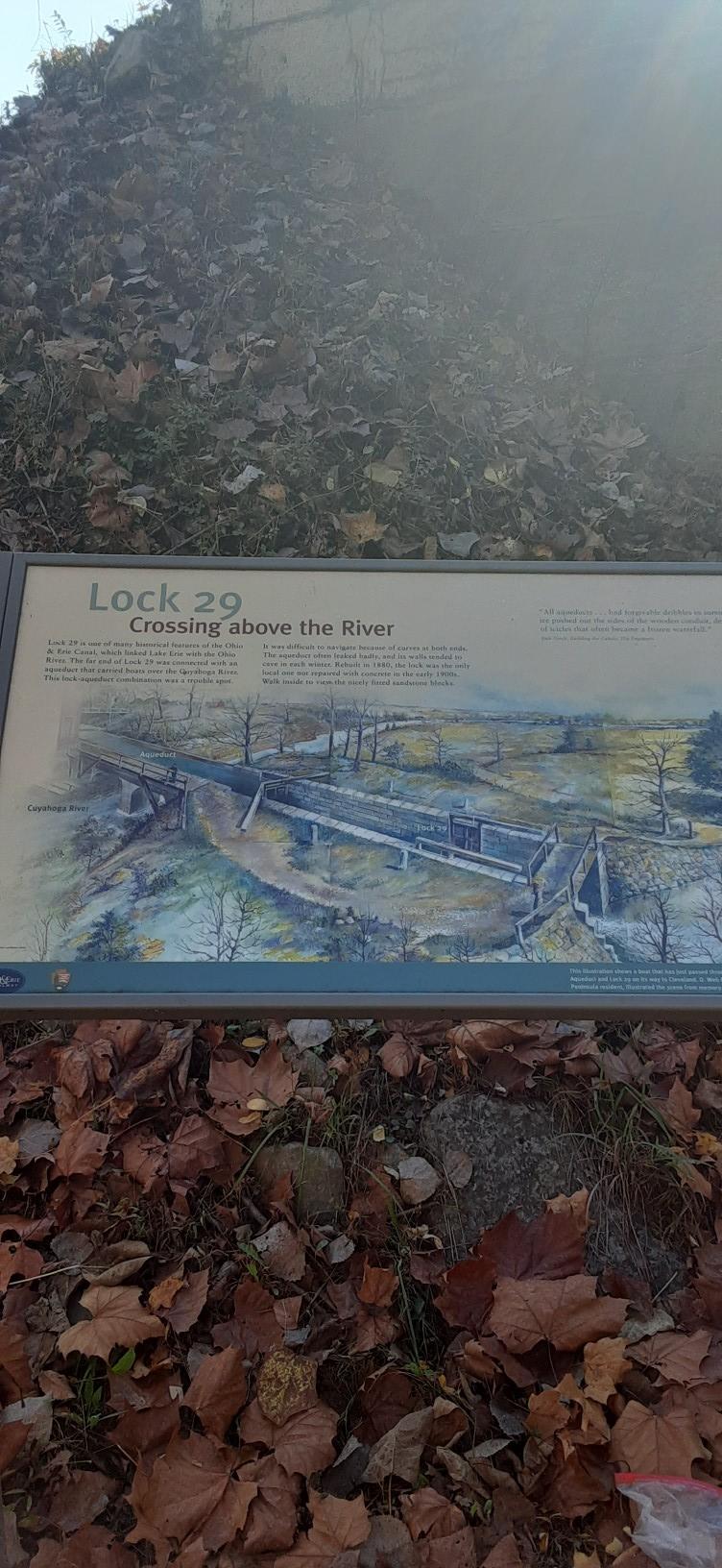 Information sign about a lock, surrounded by fallen autumn leaves on the ground.