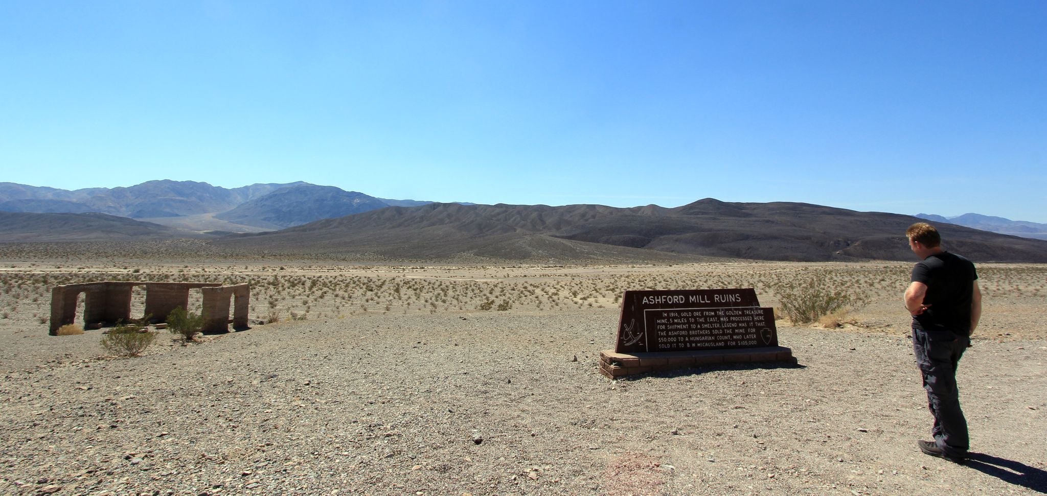Person views informational sign and ruins in a vast, sunny desert landscape. - Ashford Canyon Road