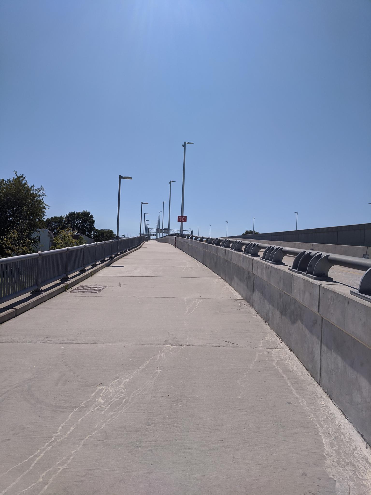 Empty concrete pedestrian walkway on a bridge under a clear blue sky.