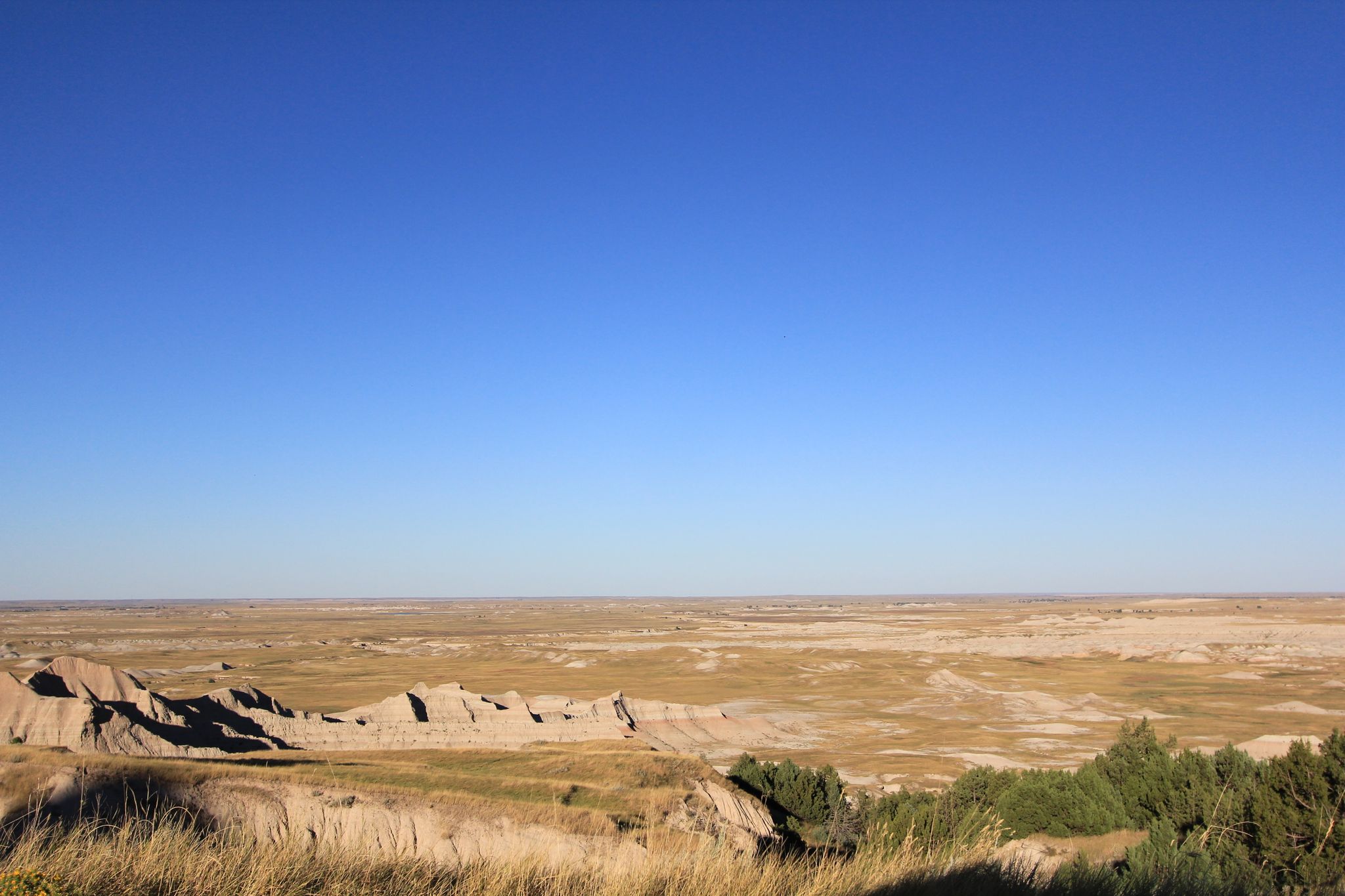 Expansive, arid landscape with distant low hills under a clear blue sky. - Badlands Loop