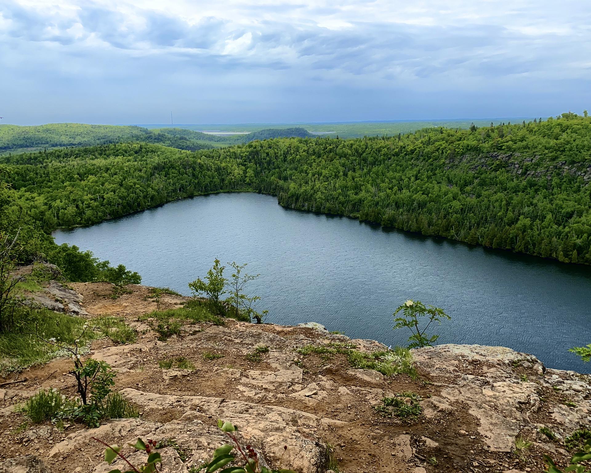 Lake surrounded by green forest under cloudy sky, from a rocky overlook.