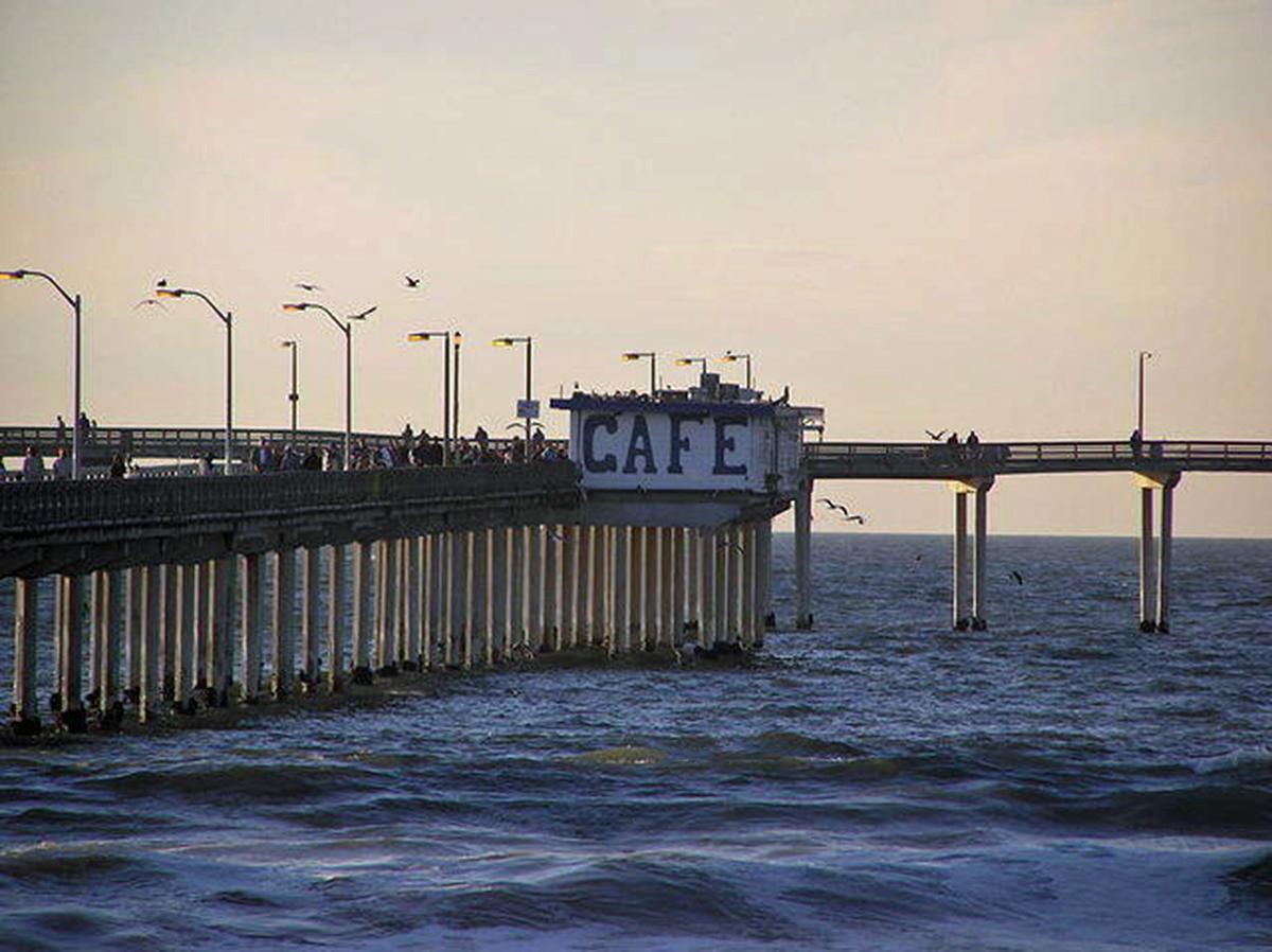 Dusk view of a pier with a cafe building and people over the ocean.