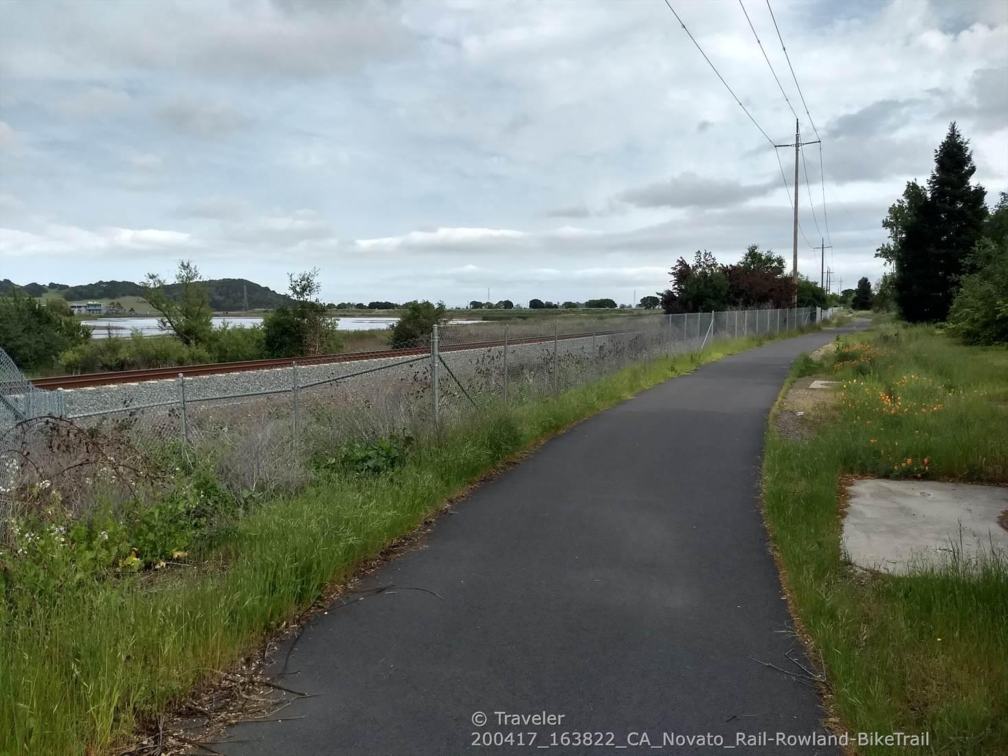 A paved path next to a chain-link fence and railroad tracks.