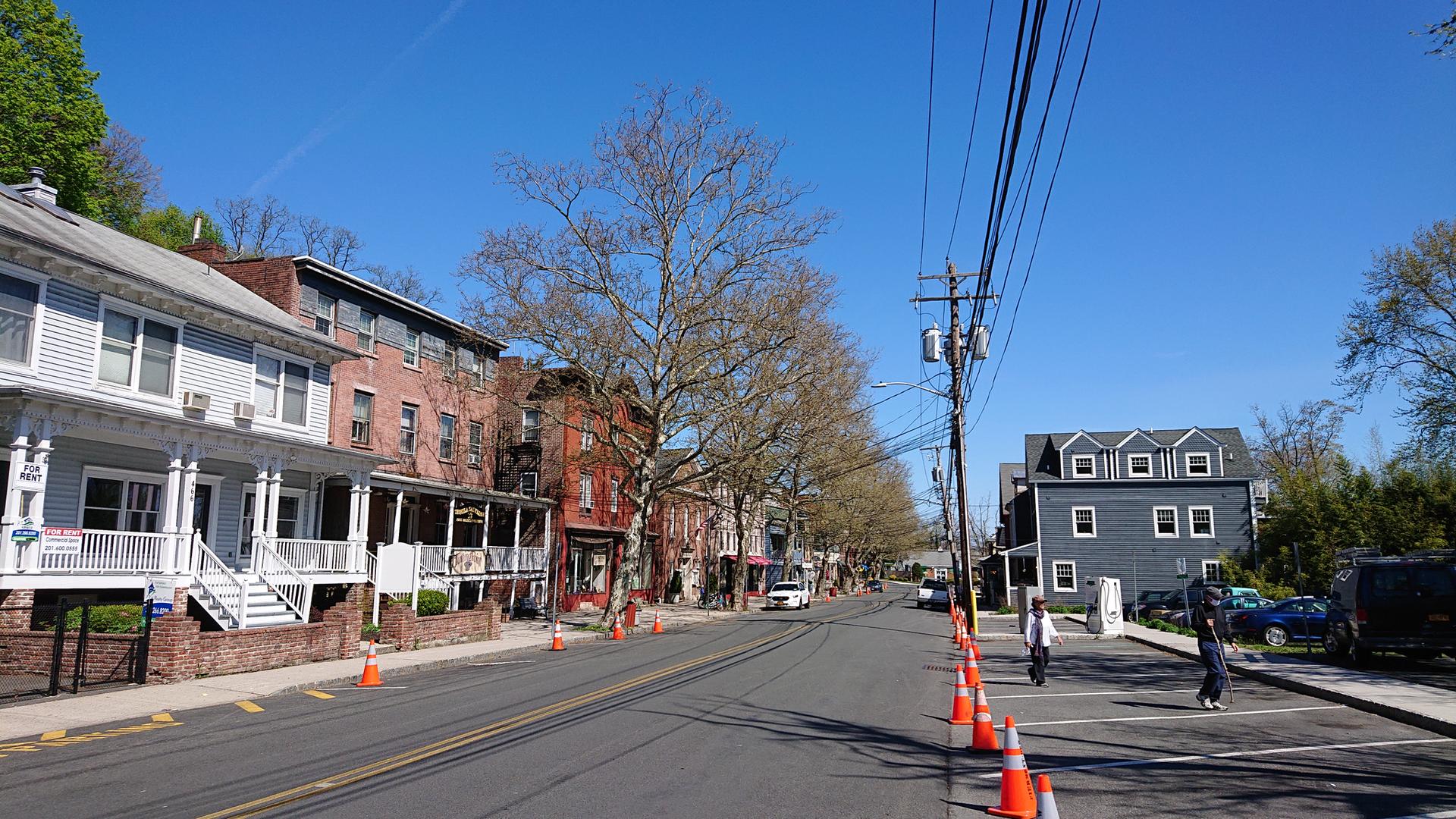 Sunny town street with buildings, bare trees, and pedestrians.