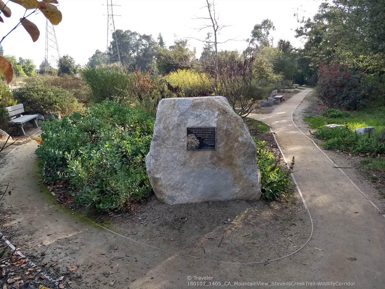 Stone monument in a sunny garden with two diverging dirt paths.
