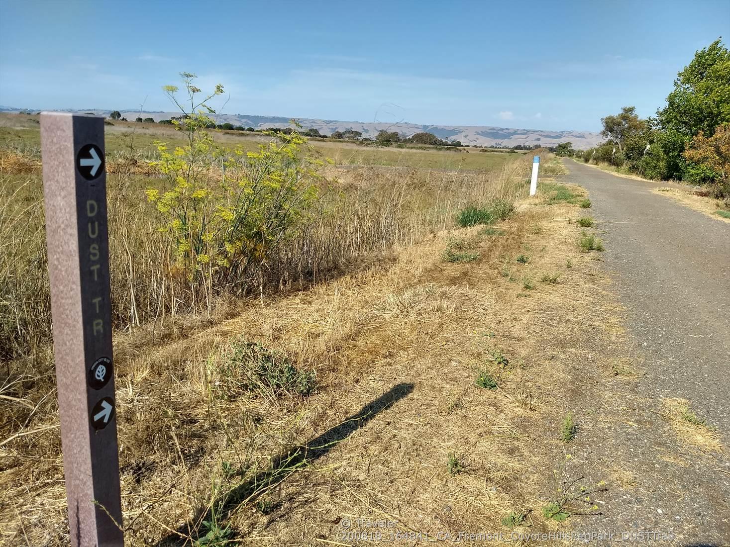 Paved path next to a trail marker in a dry, grassy field.
