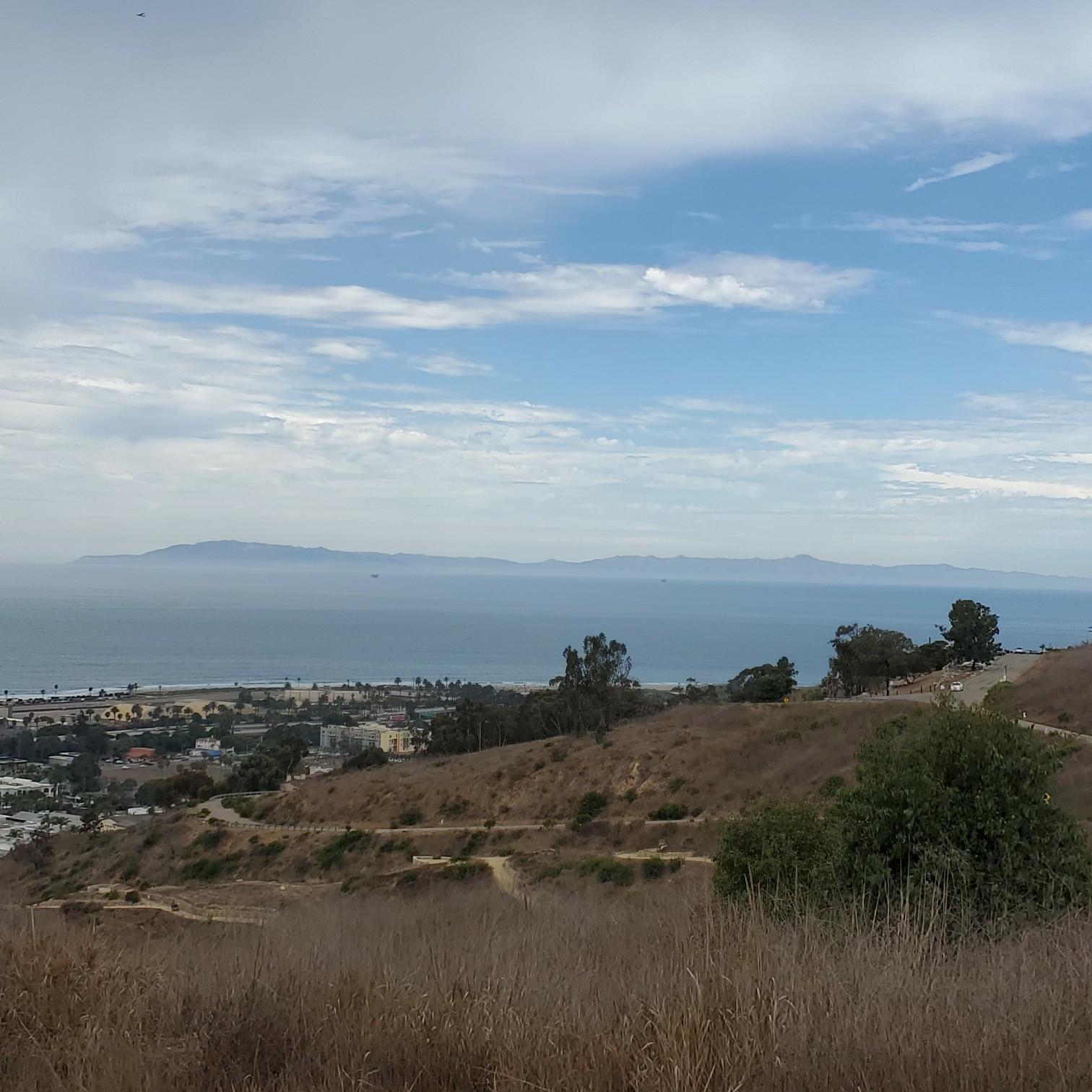Panoramic view of a coastal city, ocean, and distant islands under clouds.
