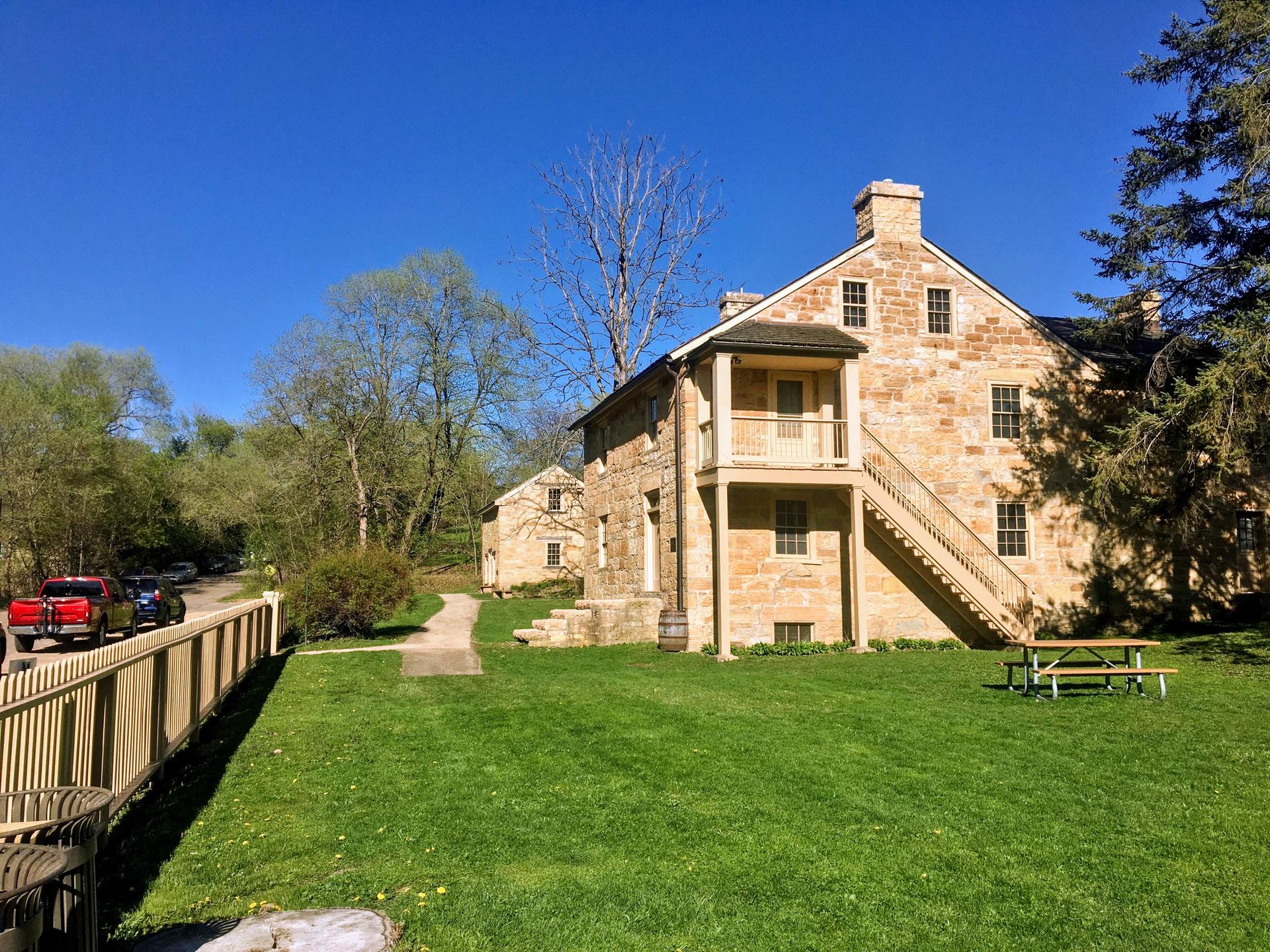 A large stone house with a porch and stairs, surrounded by a green lawn.