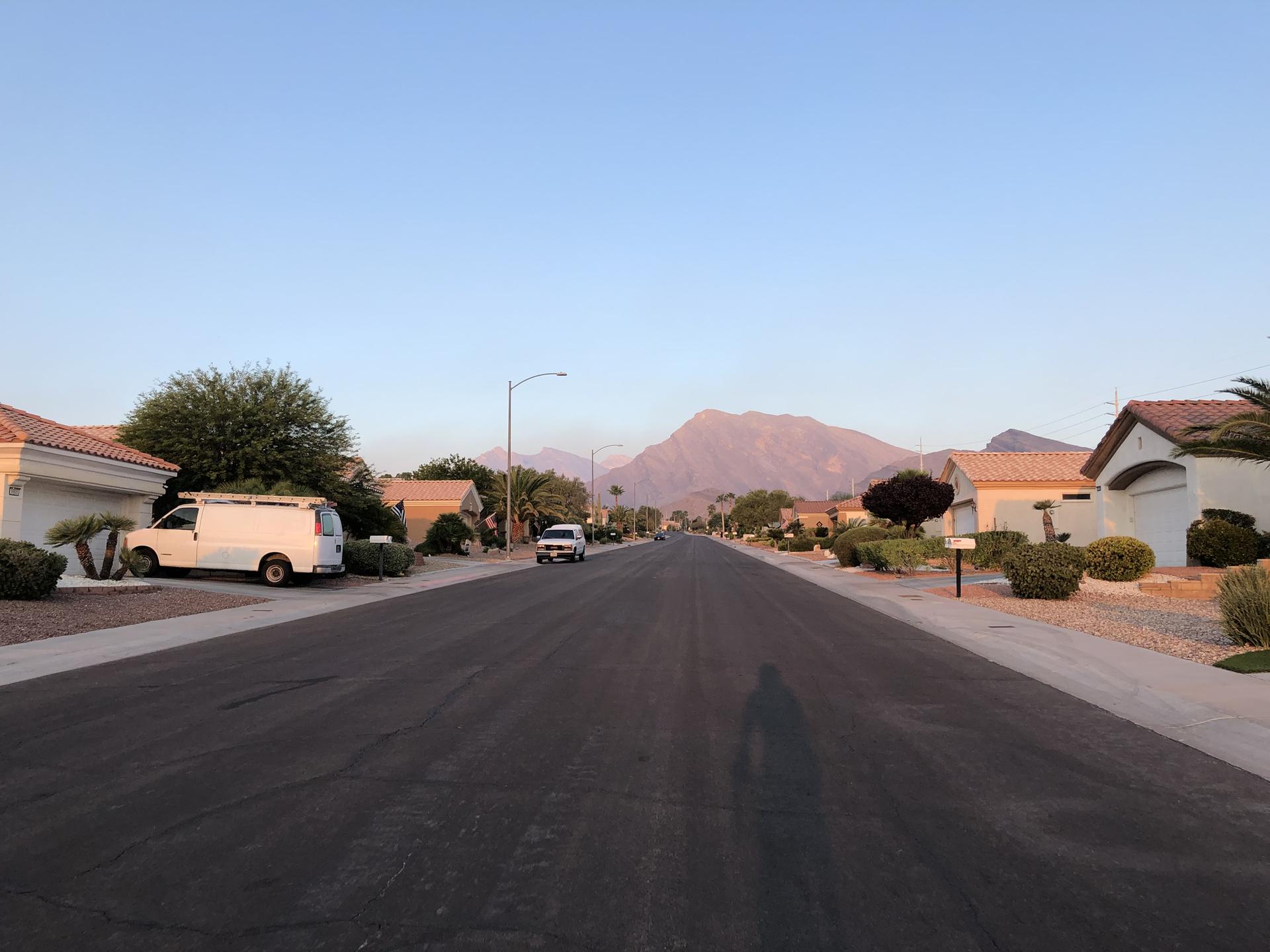 Residential street with houses, a large mountain, and a person's shadow at dusk.