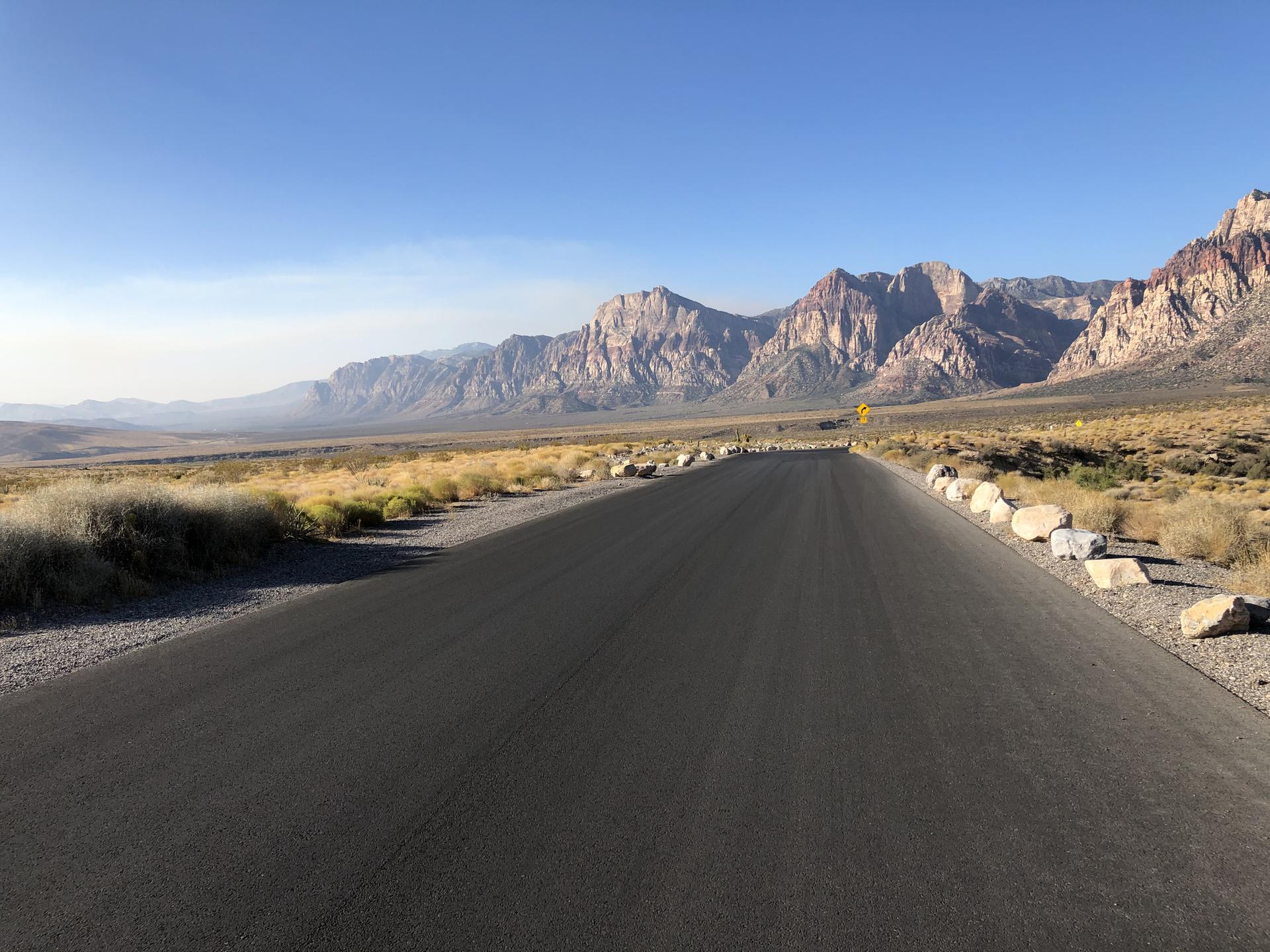 Empty paved road stretching into a desert landscape with distant mountains.