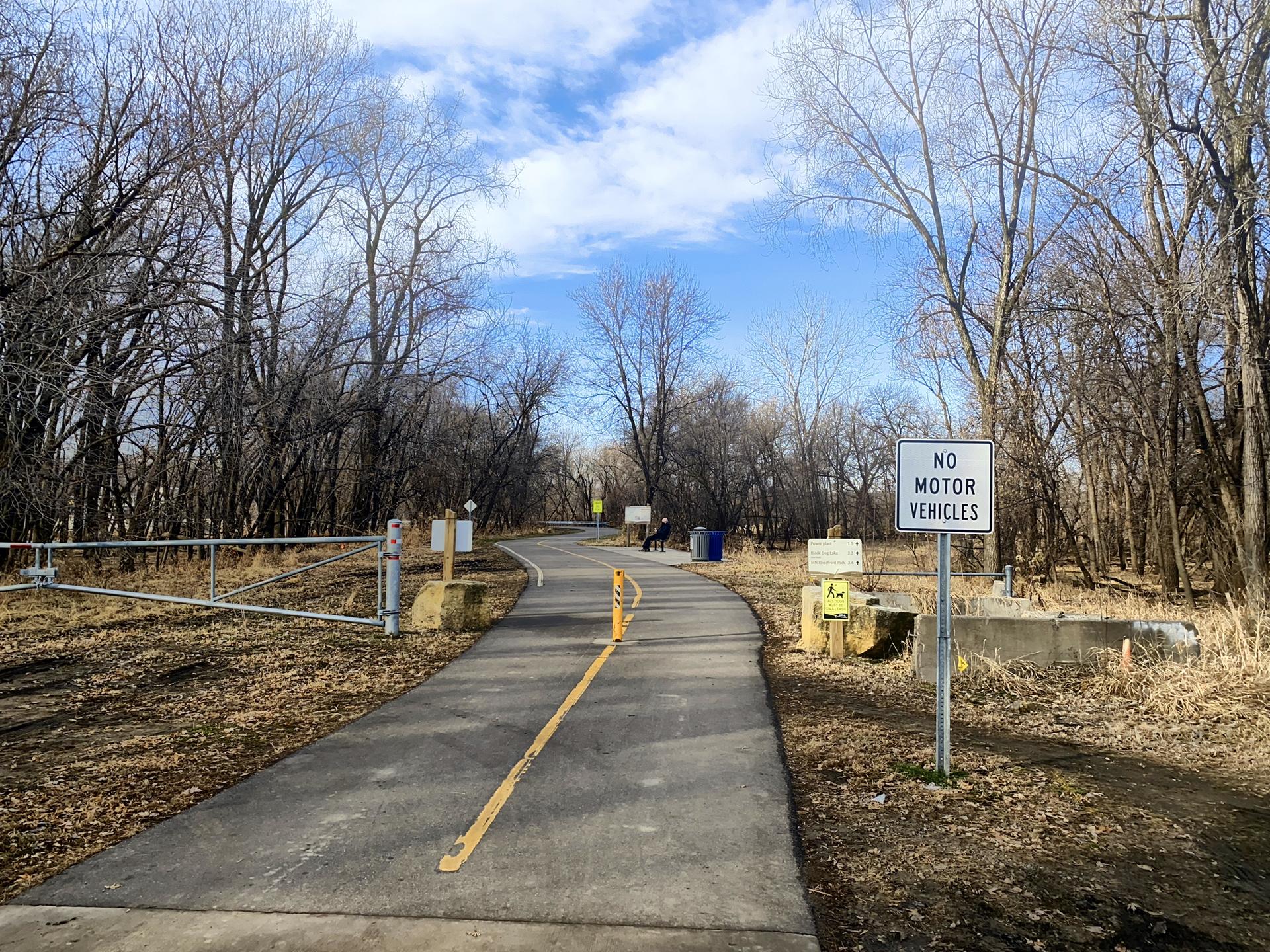 A paved trail entrance with a 'No Motor Vehicles' sign and bare trees.