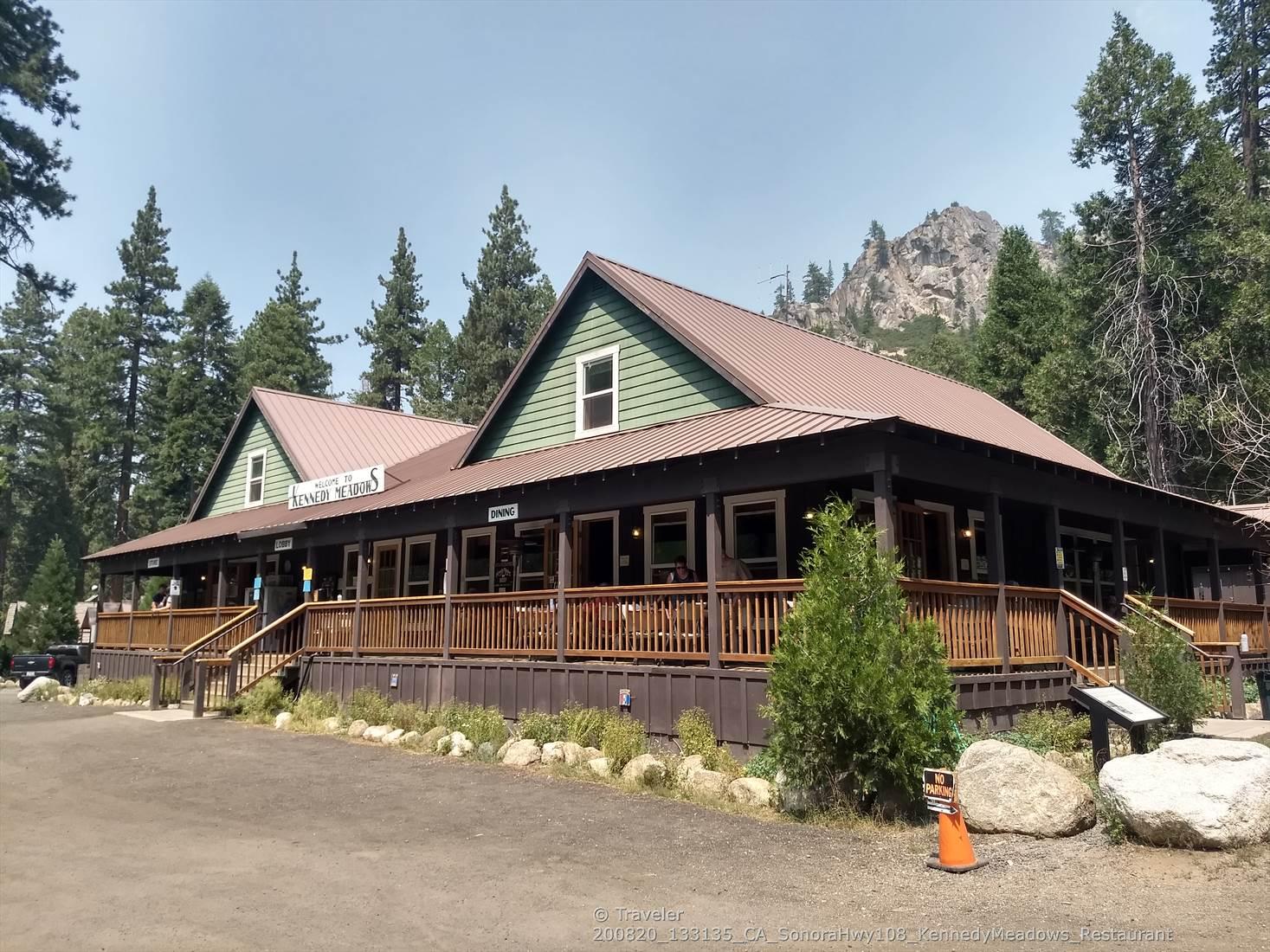 Large lodge building with a porch, surrounded by pine trees.