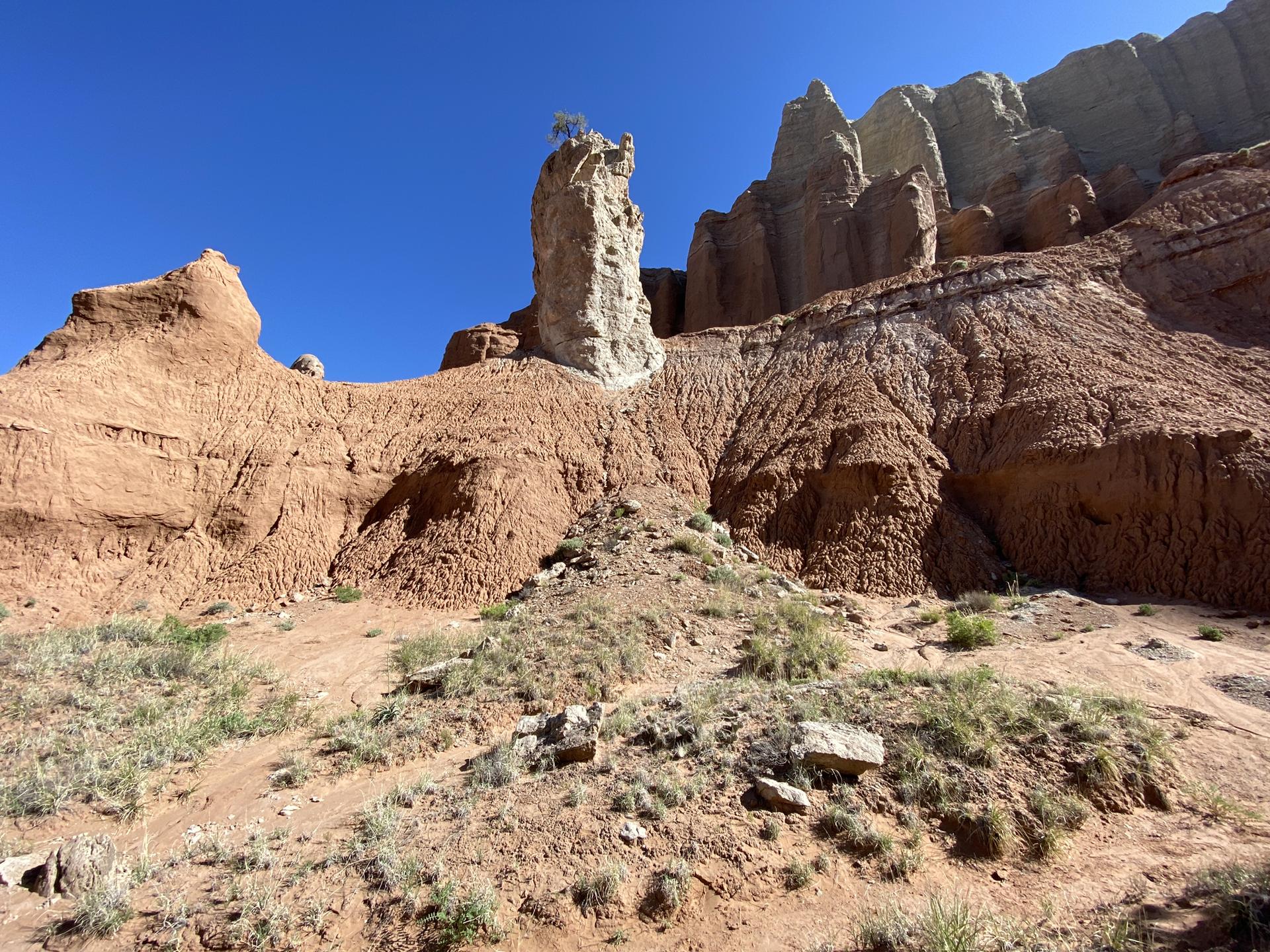 Tall white rock pillar against red cliffs under a clear blue sky.