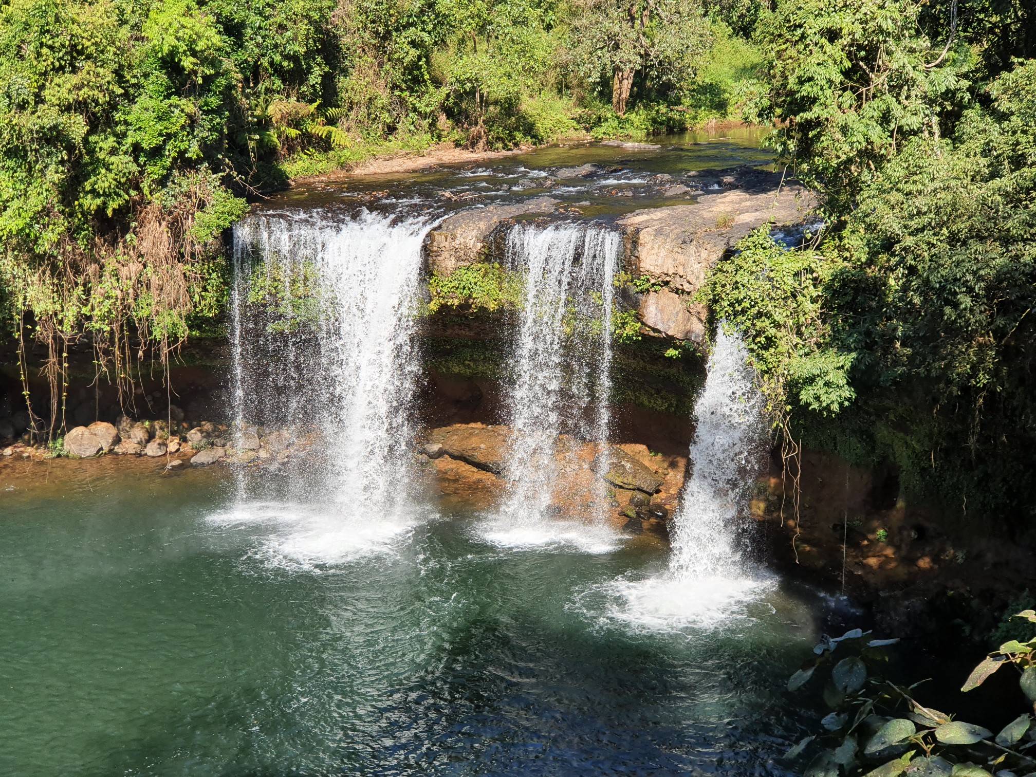 The authentic multi-tiered travertine limestone cascades of Champi Waterfall, Laos, surrounded by raw jungle foliage