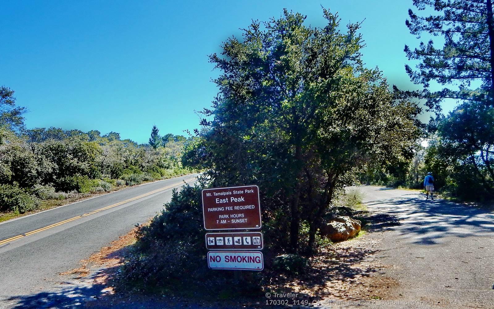 Roadside sign next to a paved road, trees, and a distant person.