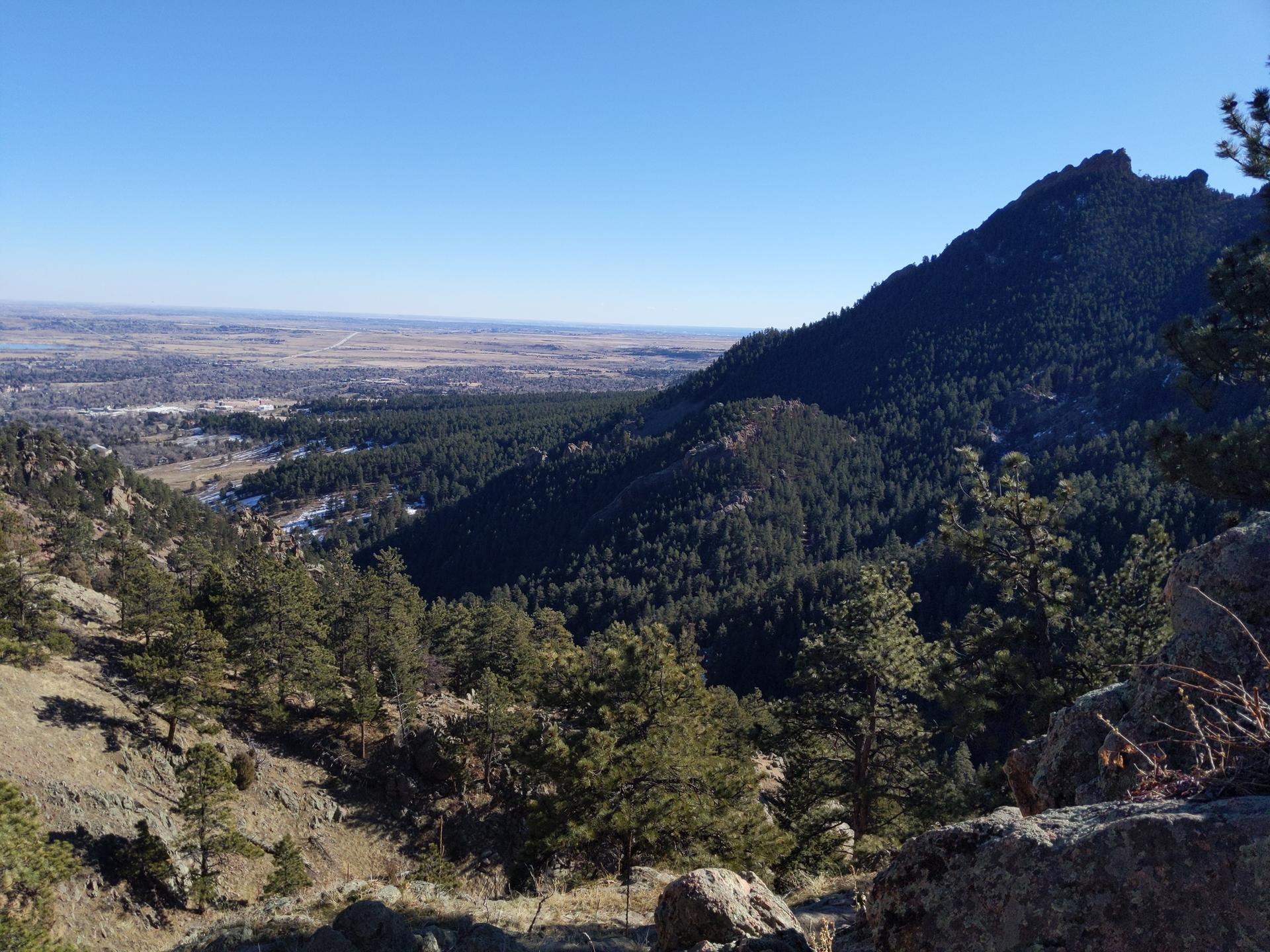 Panoramic view of a steep, forested mountain and a distant valley under clear sky.