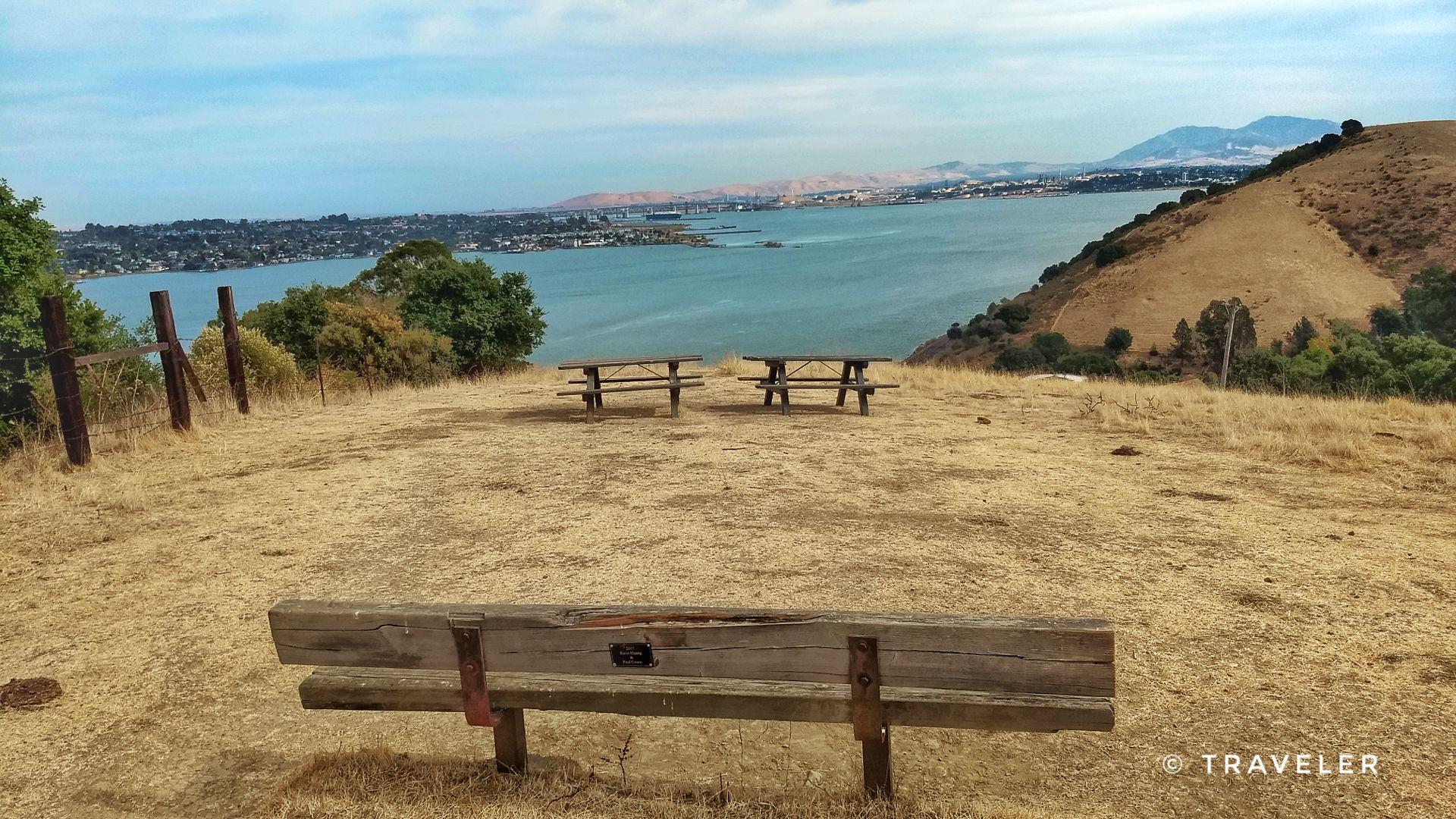 Wooden bench and picnic tables on a dry hill overlooking a large bay.