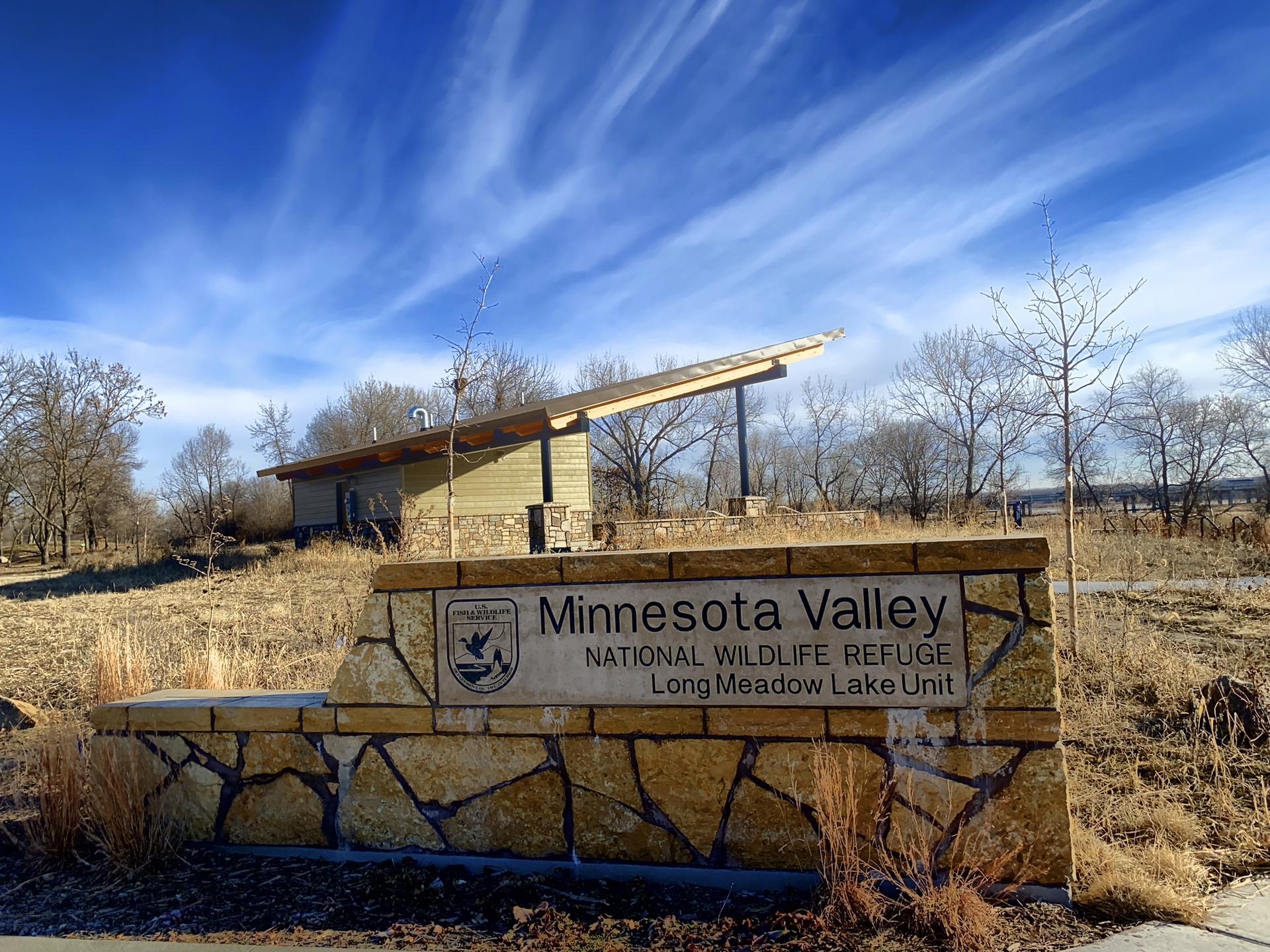 Stone sign in front of a building, surrounded by bare trees under a blue sky.