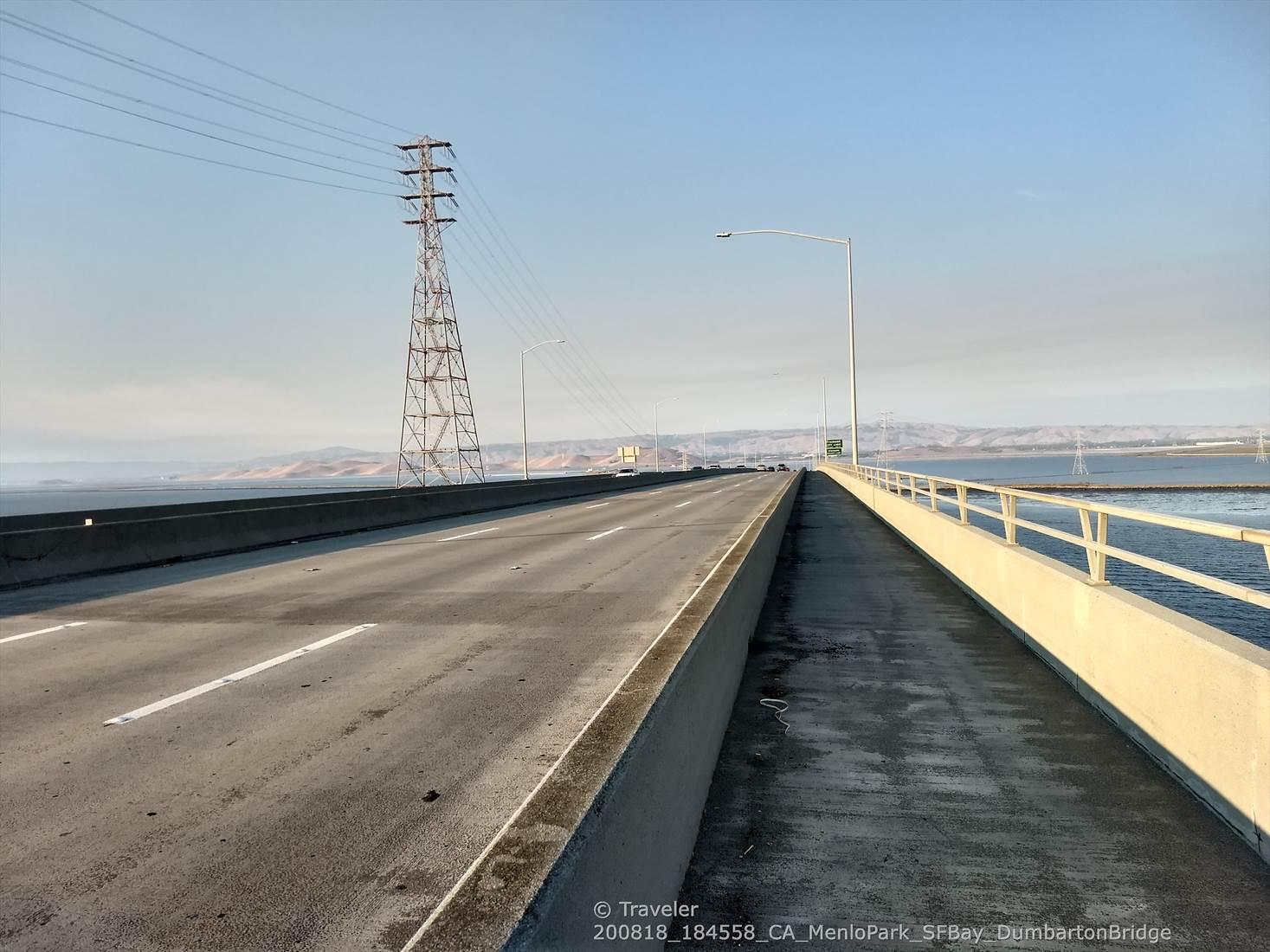 A long, empty bridge stretches over water under a bright, clear sky.