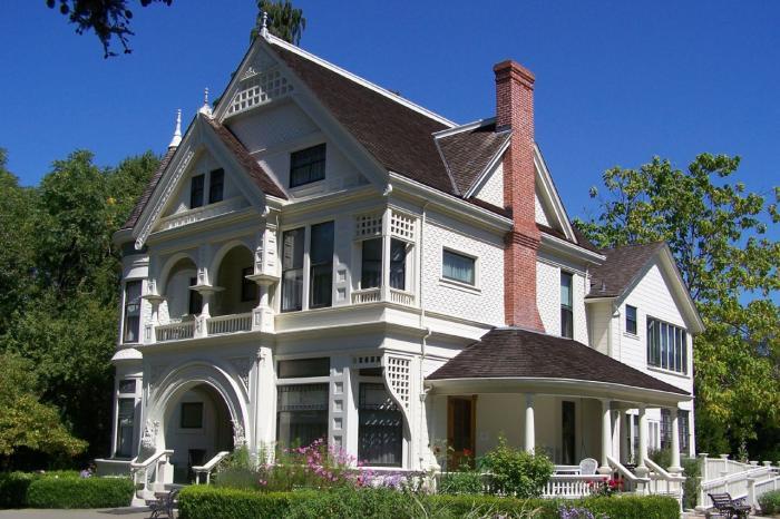 A grand white Victorian house with a red chimney and lush green garden.