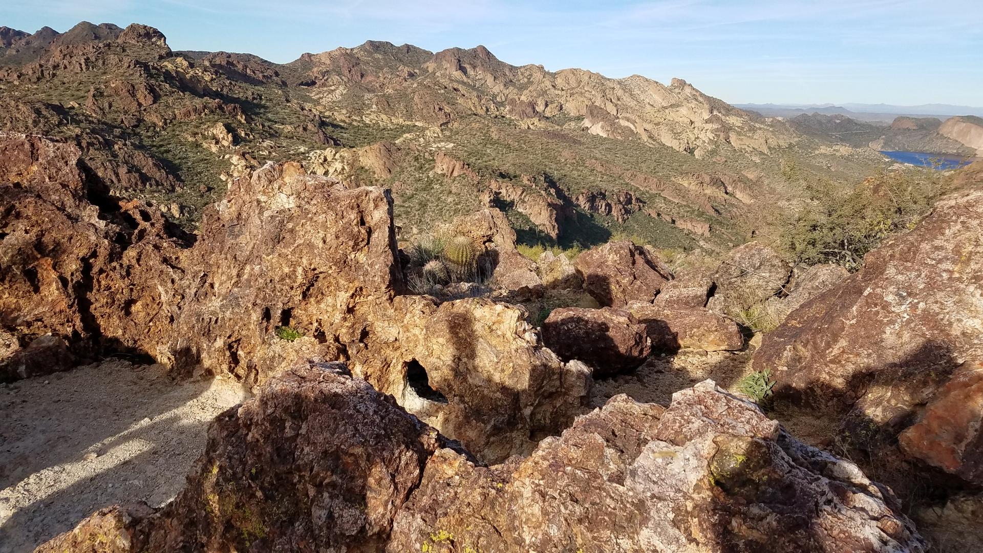 Rugged, rocky foreground overlooking arid mountains and a distant lake under clear skies.