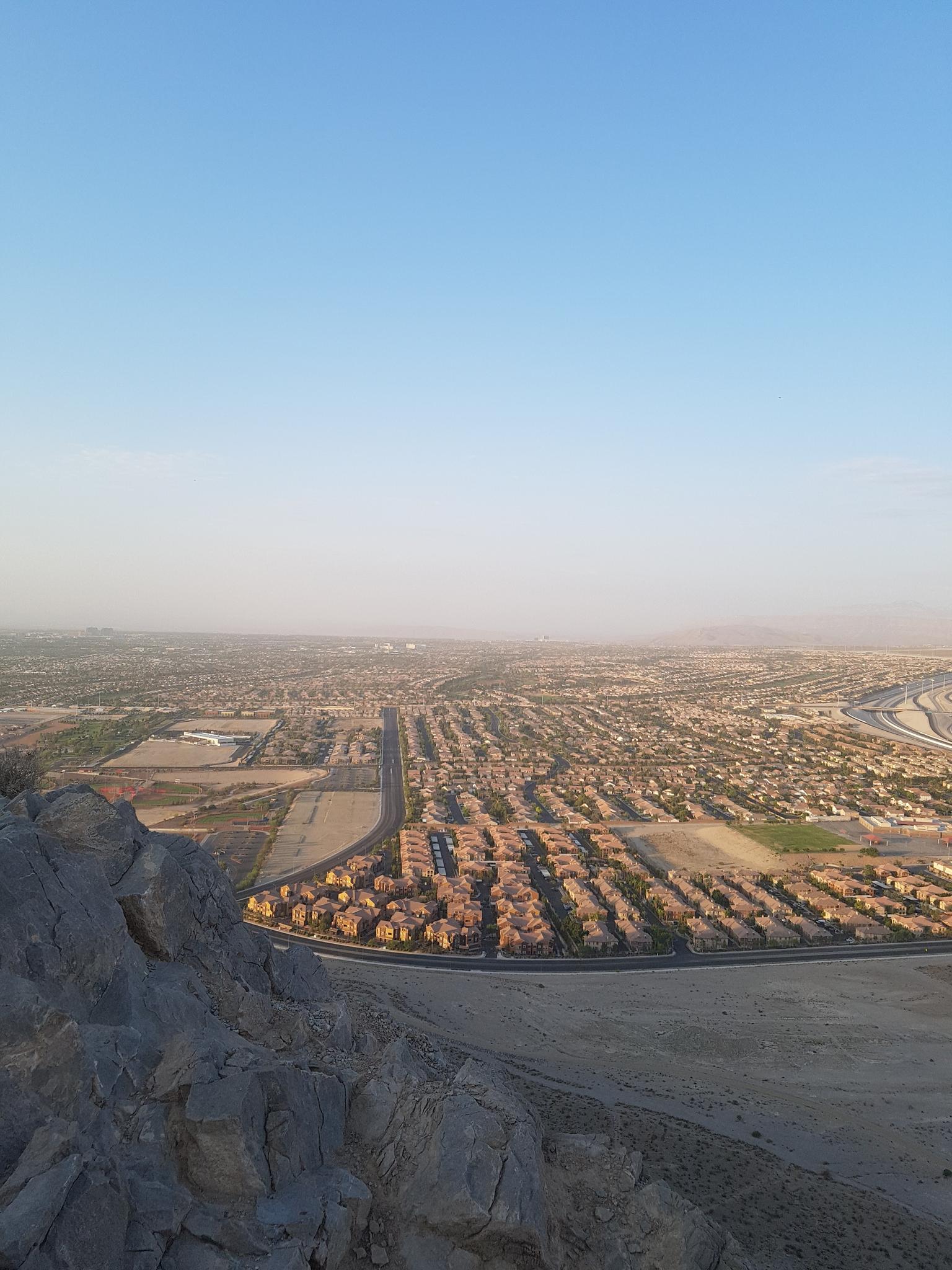 Elevated view of a vast city sprawling into a hazy desert horizon at dawn.
