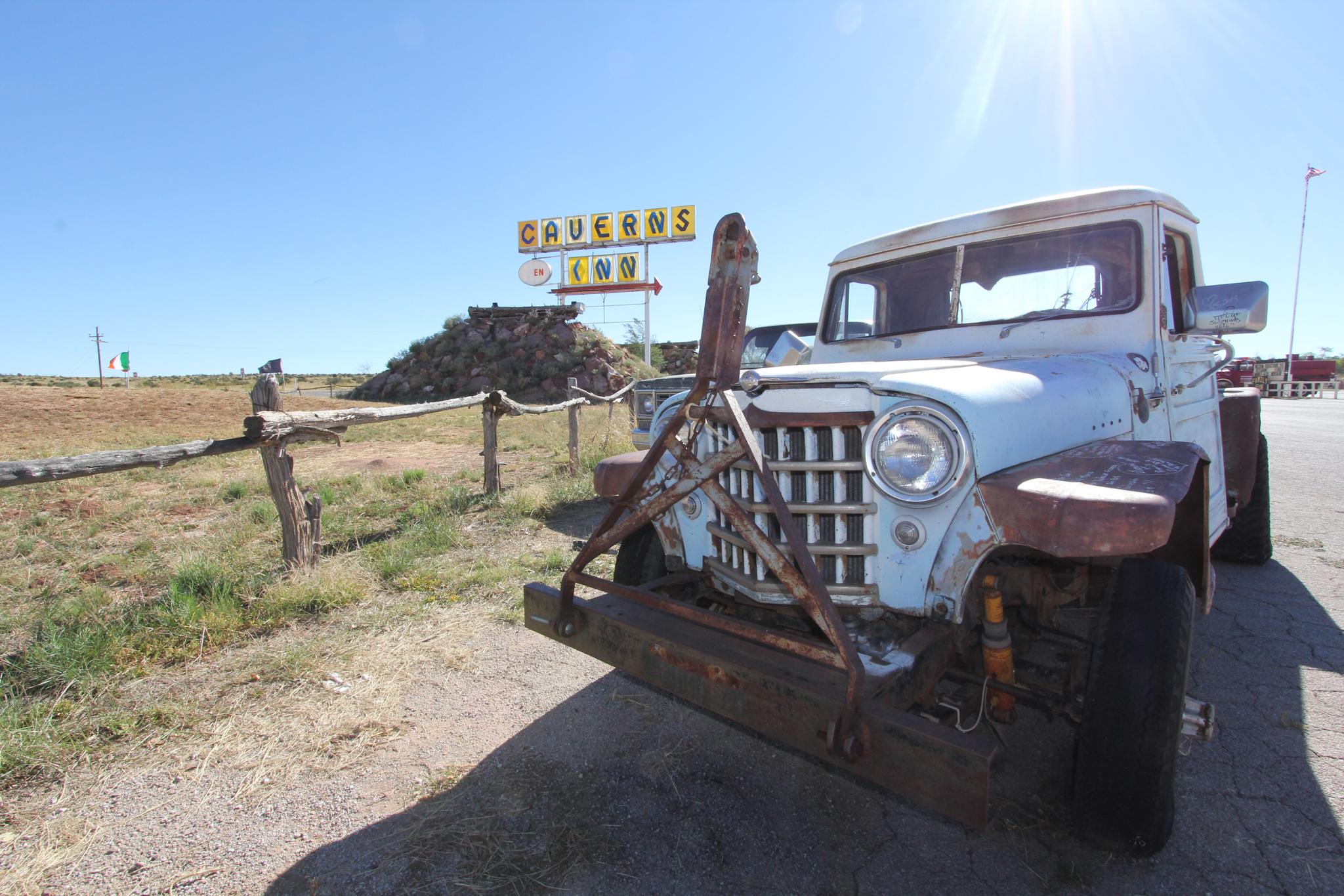 Old white pickup truck with a plow attachment under bright sun.