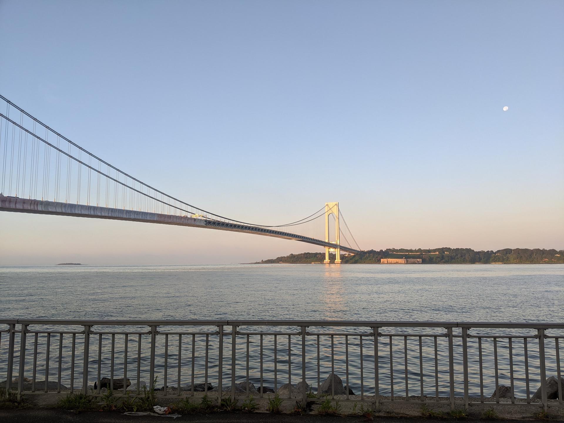 A large suspension bridge spans calm water under a soft, clear sky.