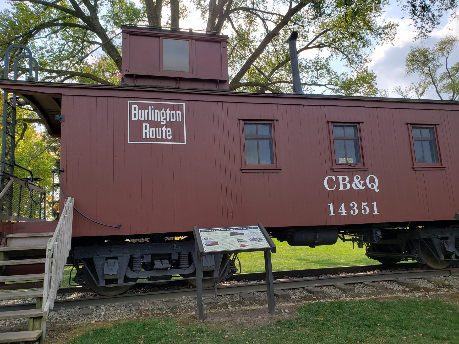 A red historical train caboose on tracks with a sign nearby.