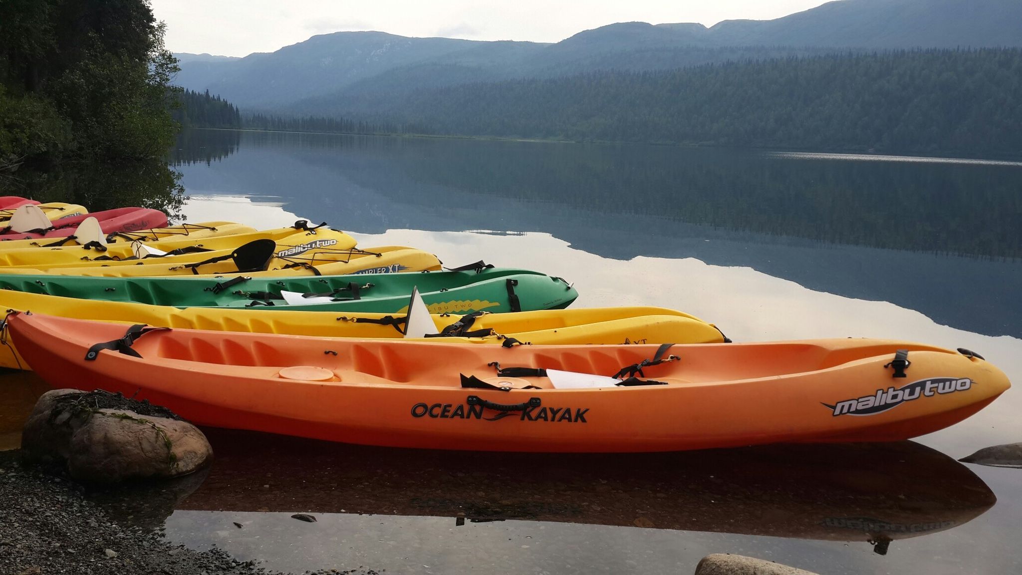 Colorful kayaks rest on a lake shore with mountains and reflections in the water. - Byers Lake Loop Trail