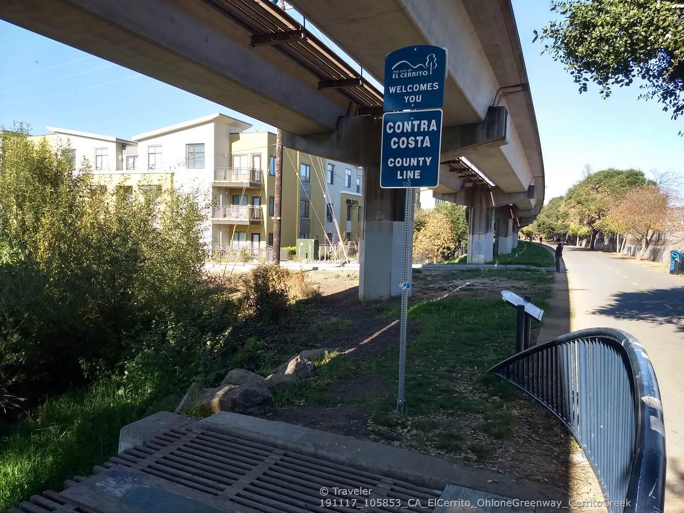 Elevated concrete structure with signs overlooks a paved path and apartment building.