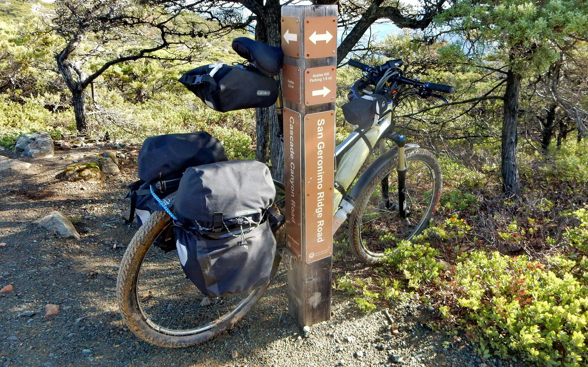 A touring mountain bike with panniers parked next to a wooden trail sign.