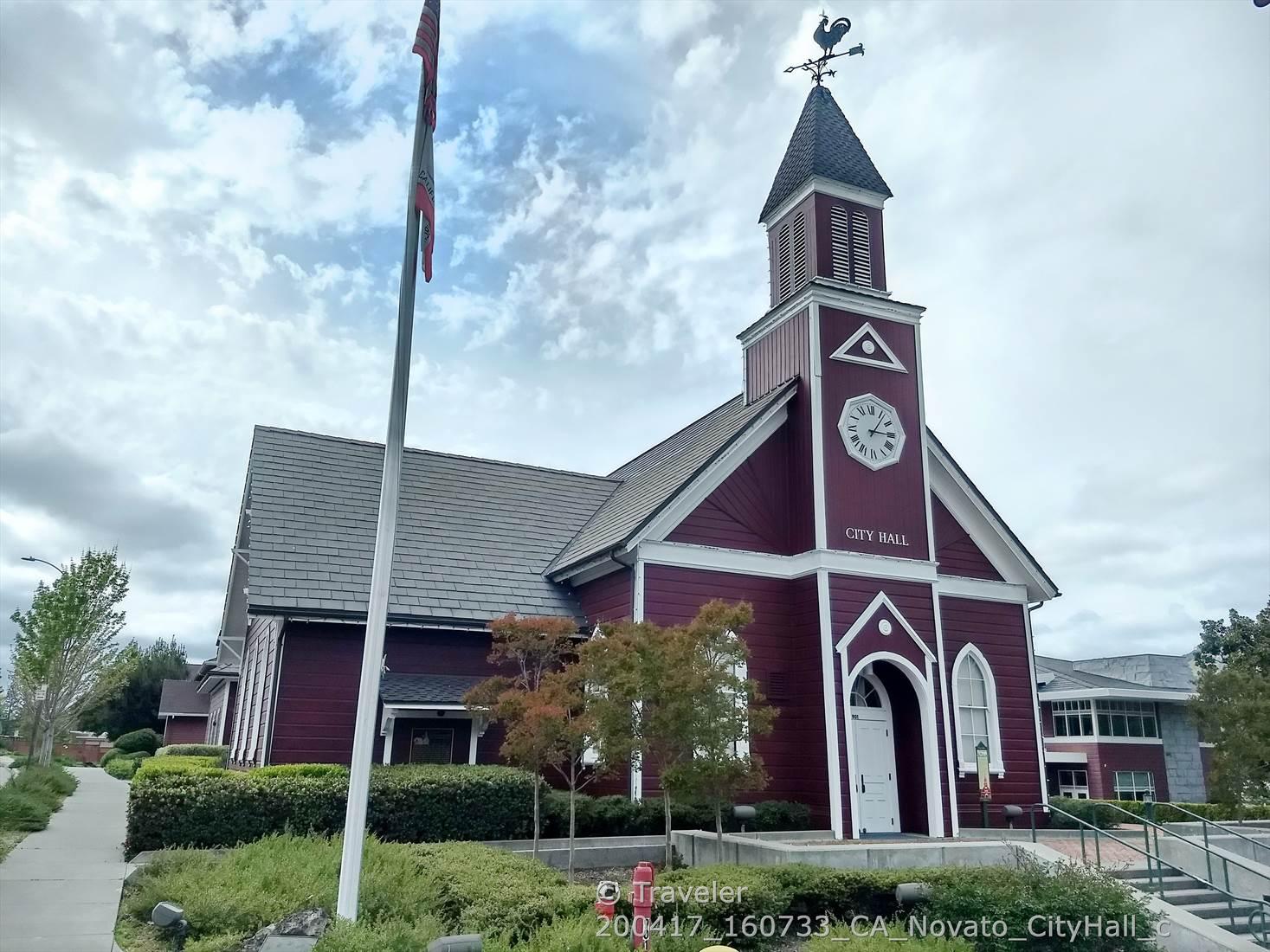Red building with a clock tower, weathervane, and flagpole under cloudy sky.